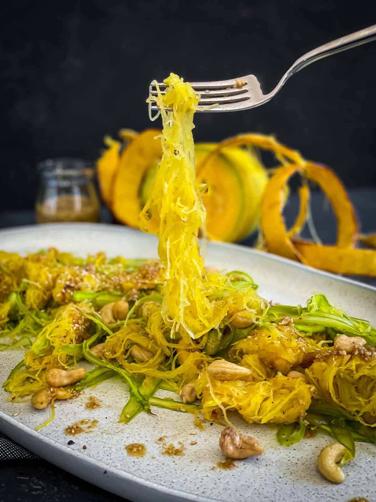 A fork lifting spaghetti squash from salad with asparagus