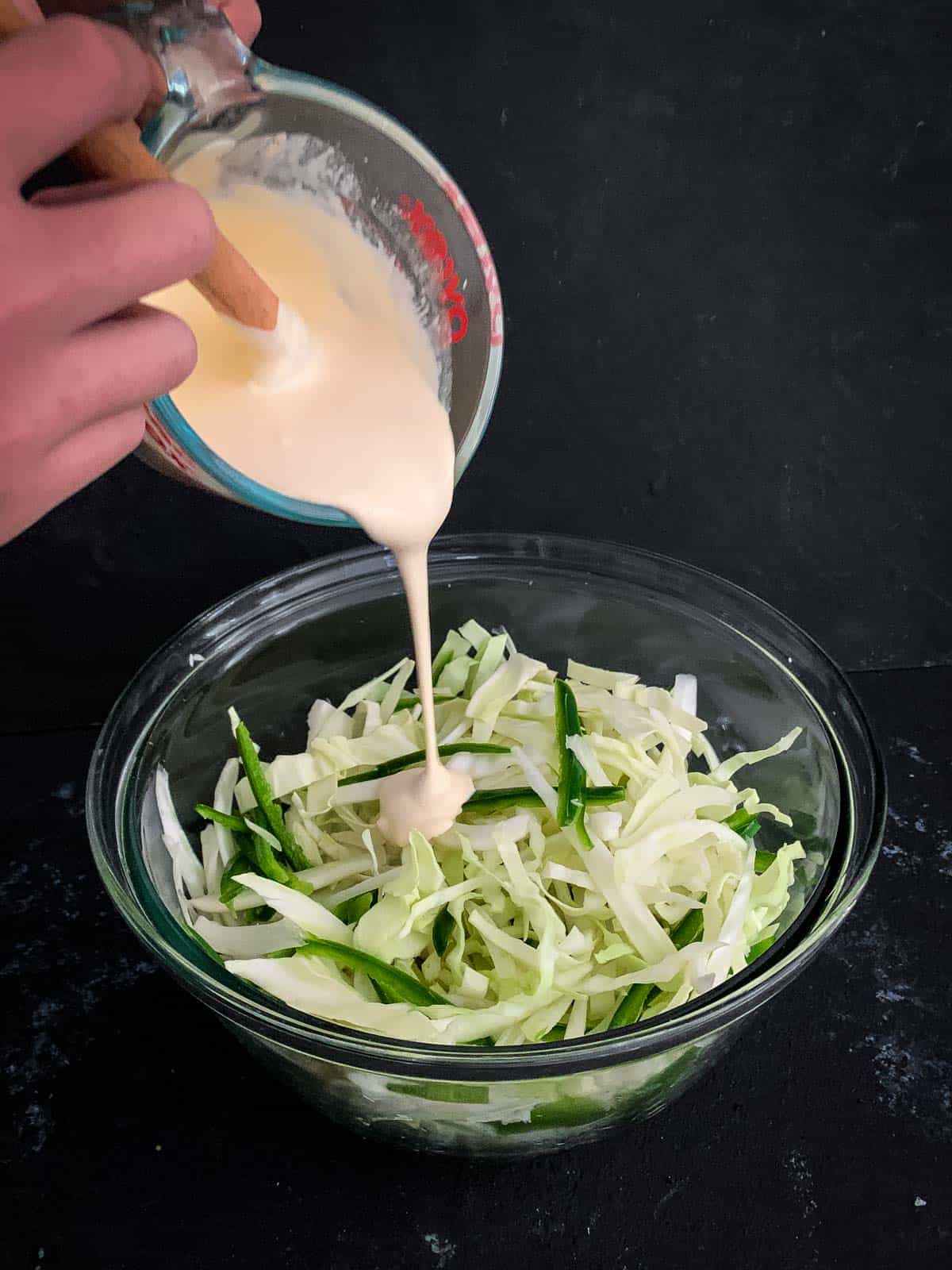 Pouring coleslaw dressing into a mixing bowl of coleslaw vegetables