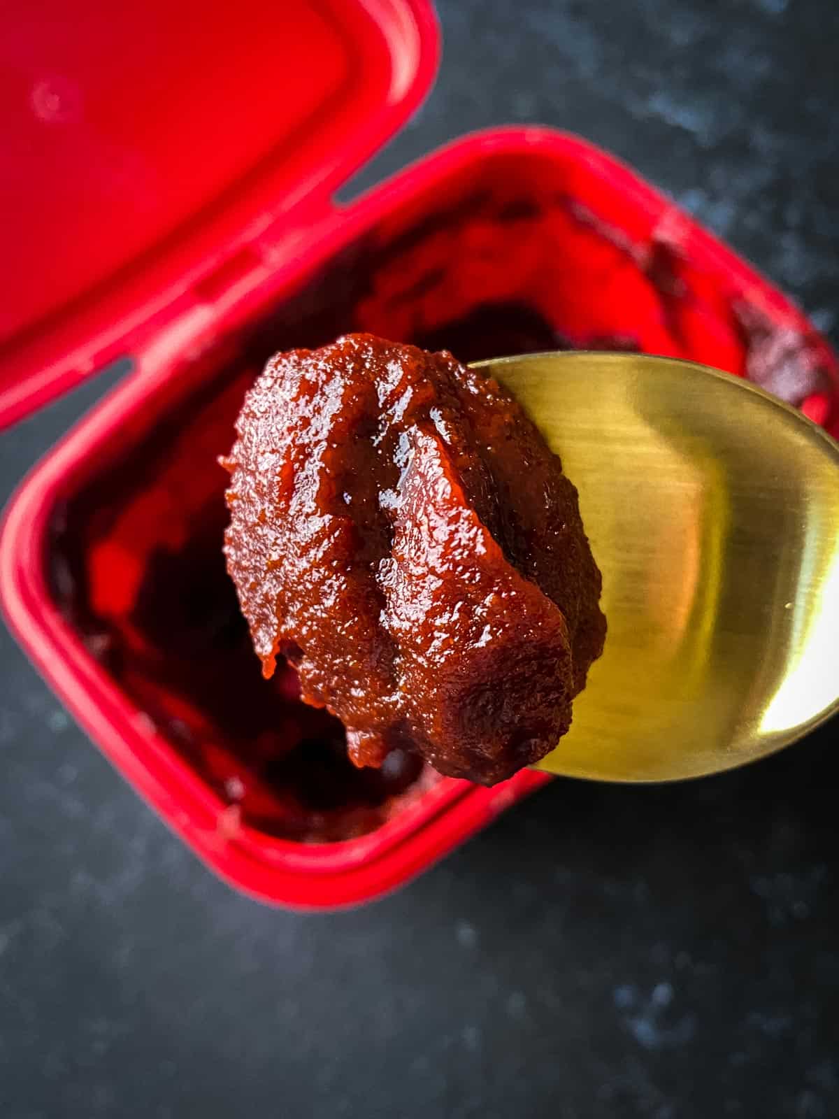 Gold spoon scooping up a serve of gochujang paste from the container