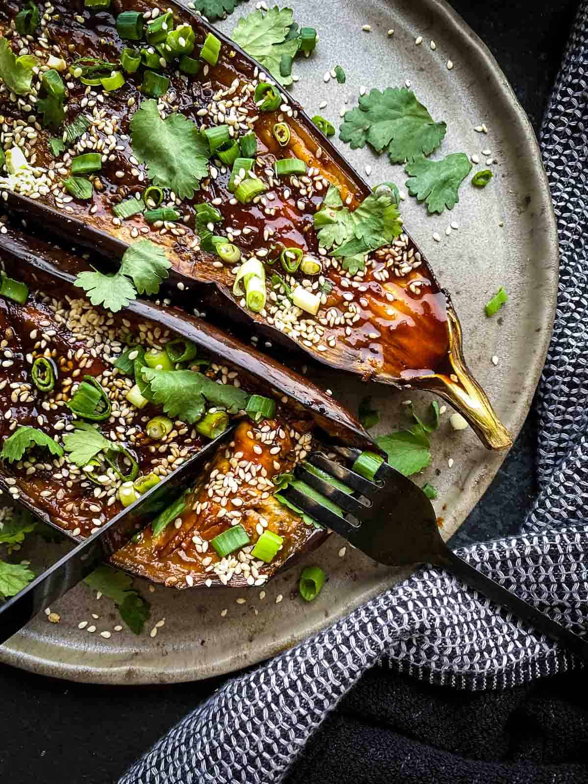 Roasted Asian Eggplant with Gochujang Glaze on a brown plate with black cutlery