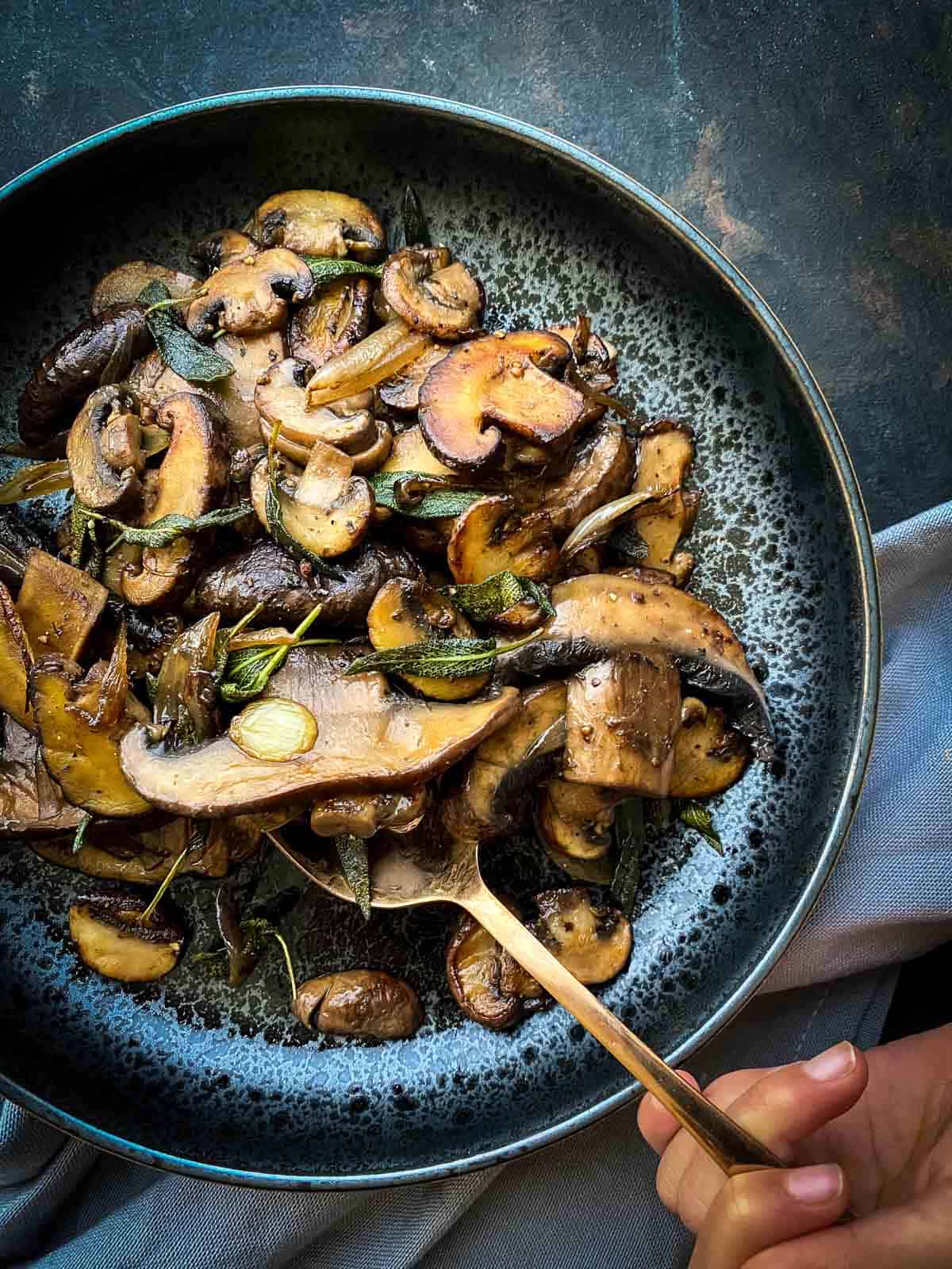 Hand with gold spoon getting a serve of Easy Sauteed Mushrooms with Soy Sage Butter