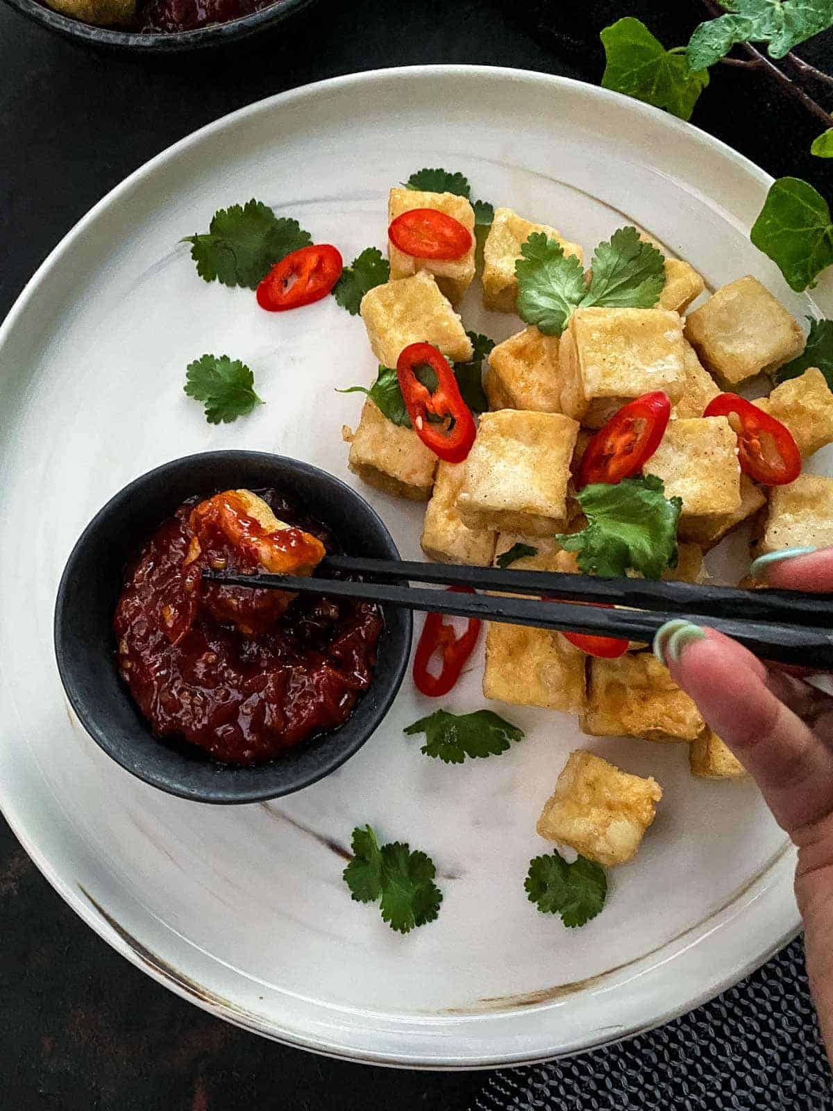 Dipping salt and pepper tofu into sweet chilli jam with chopsticks