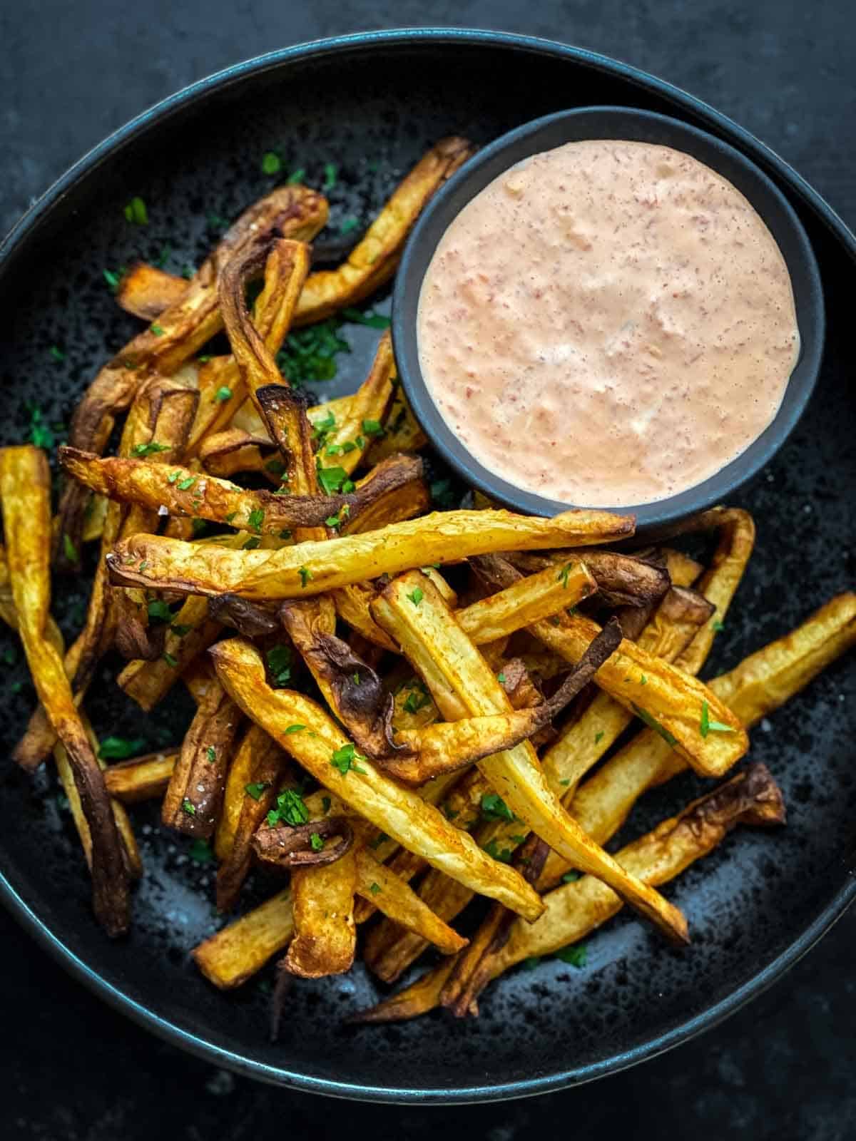 Air Fryer Parsnip Fries in a black speckled bowl with red pepper mayo sauce