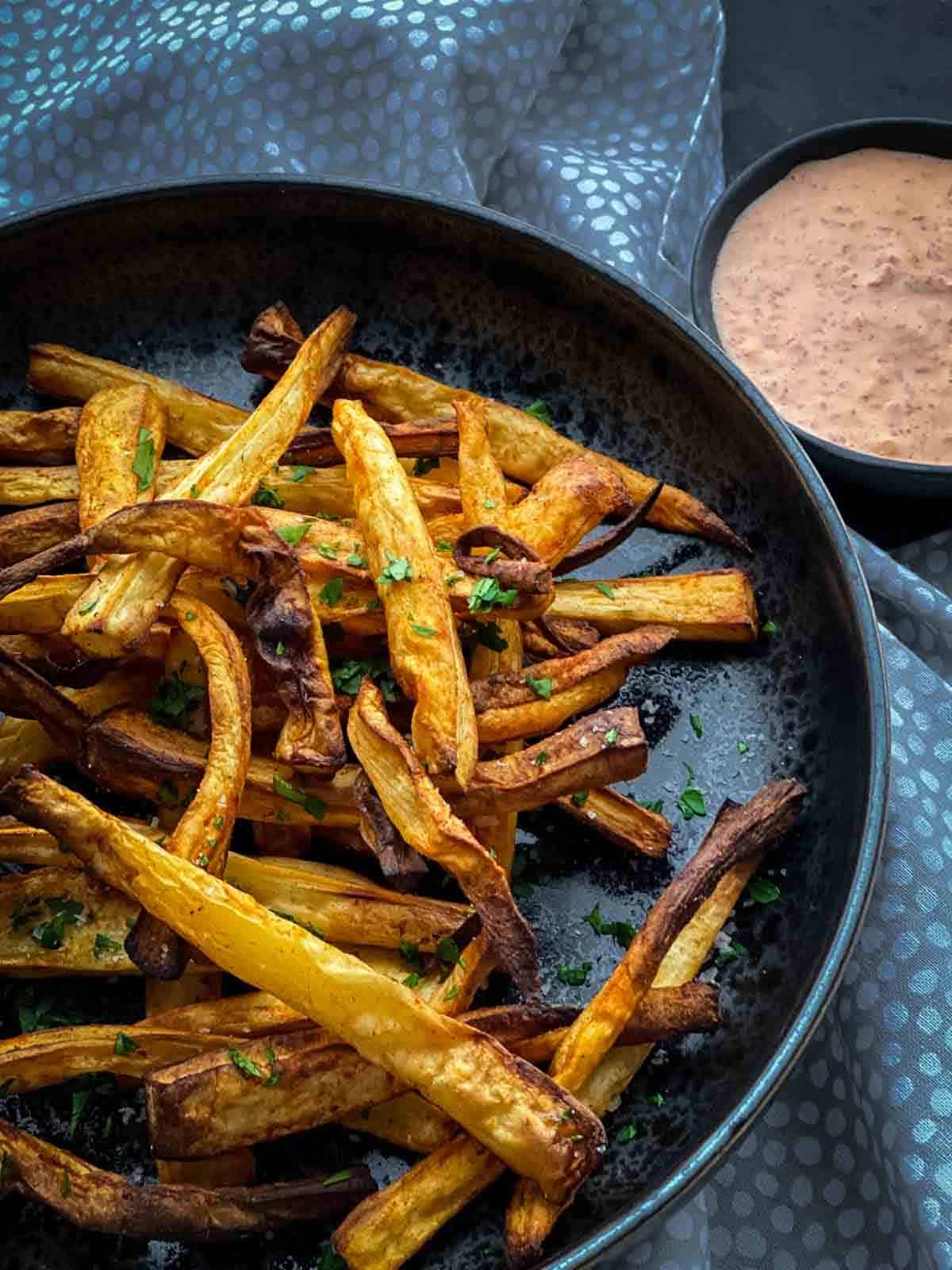 Air Fryer Parsnip Fries in a black speckled bowl with red pepper mayo sauce and dotted napery