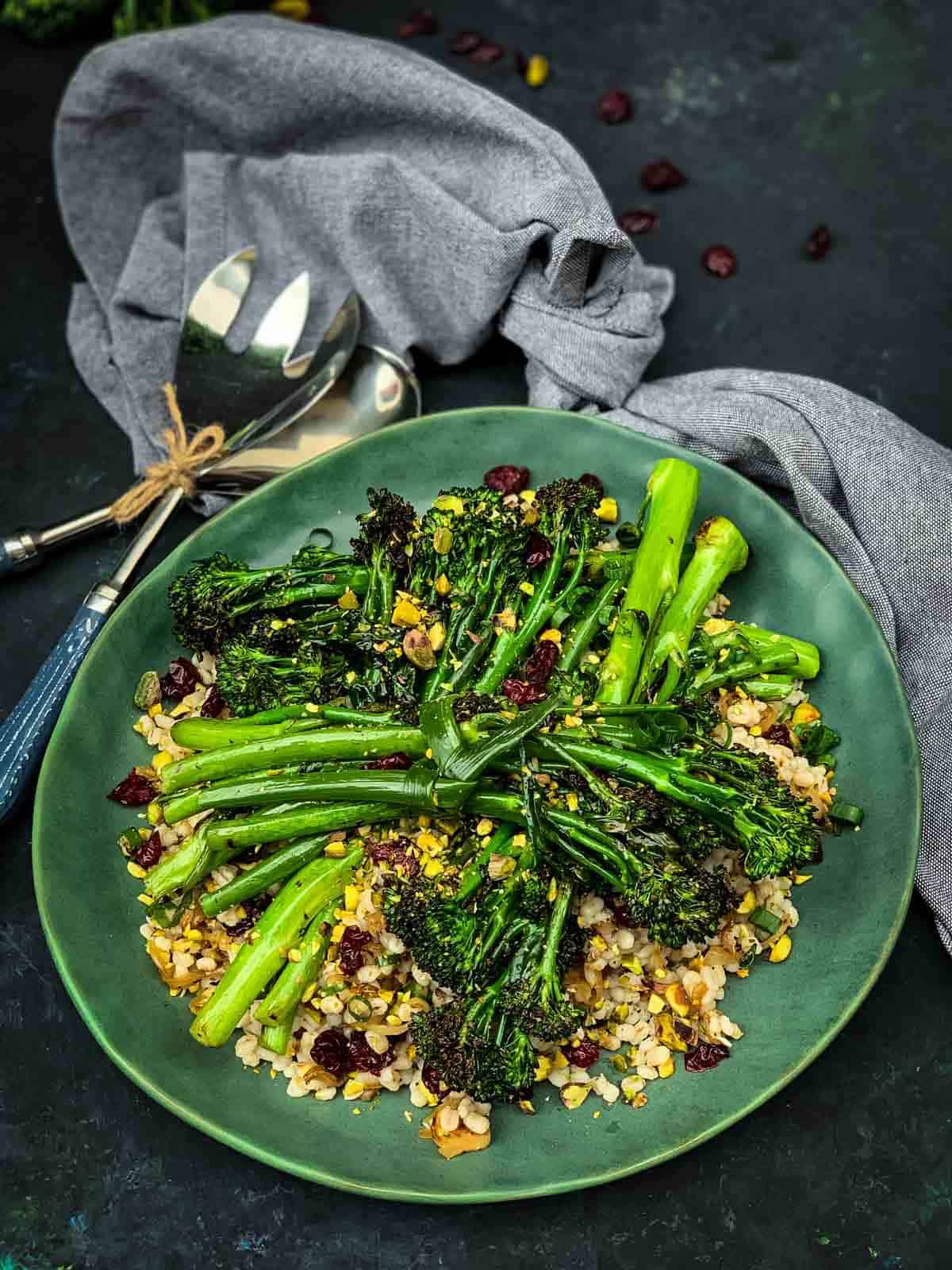 Grilled Broccolini Salad and Barley on a green plate with grey napery and blue salad servers