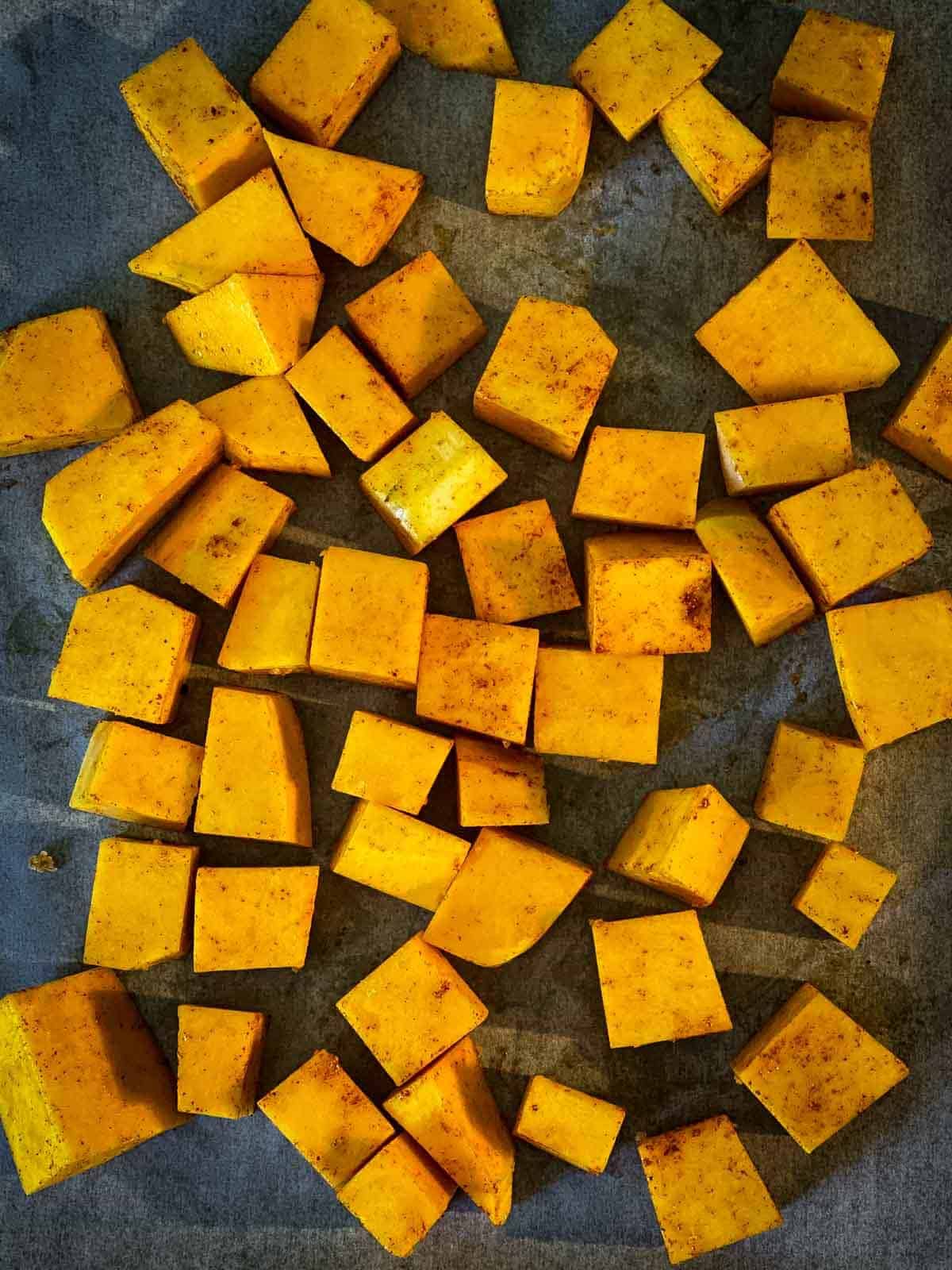 Cubes of spiced butternut squash on a sheet pan ready for roasting