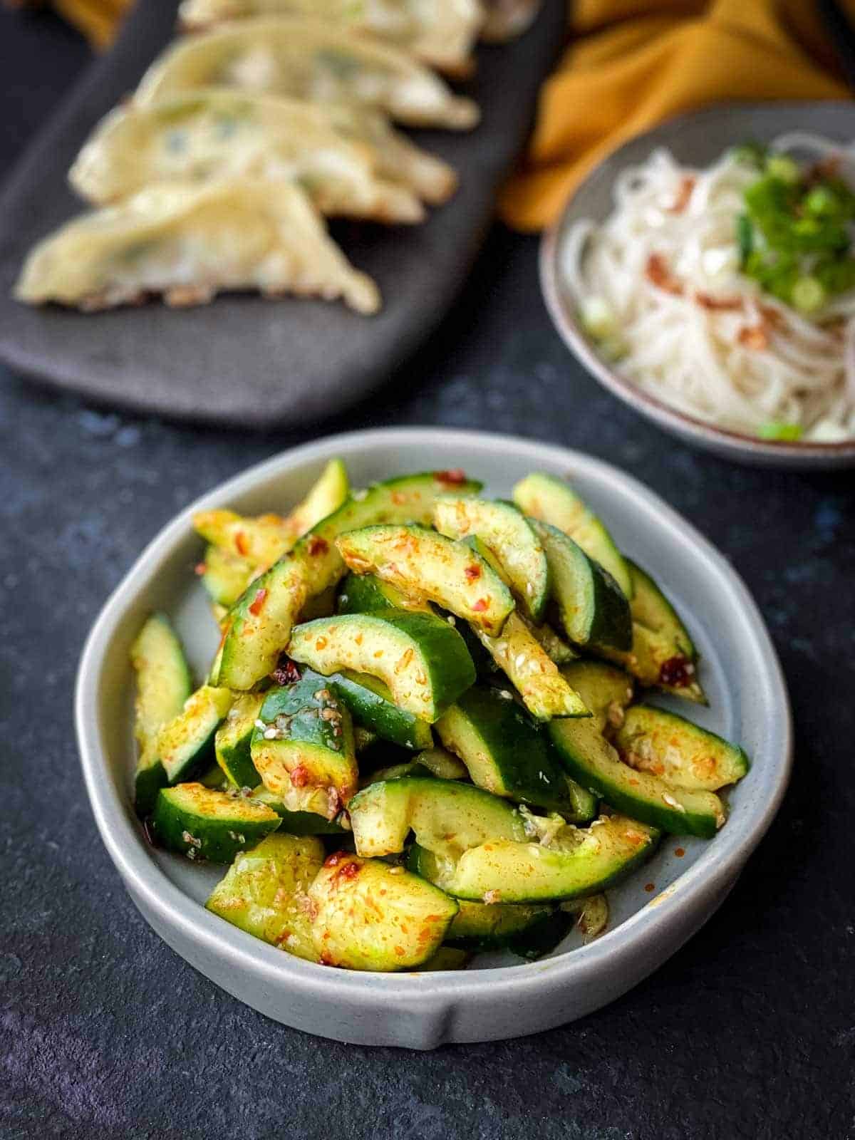 Chinese Smashed Cucumber Salad (Pai Huang Gua) in a small grey bowl served with fried dumplings and noodles.