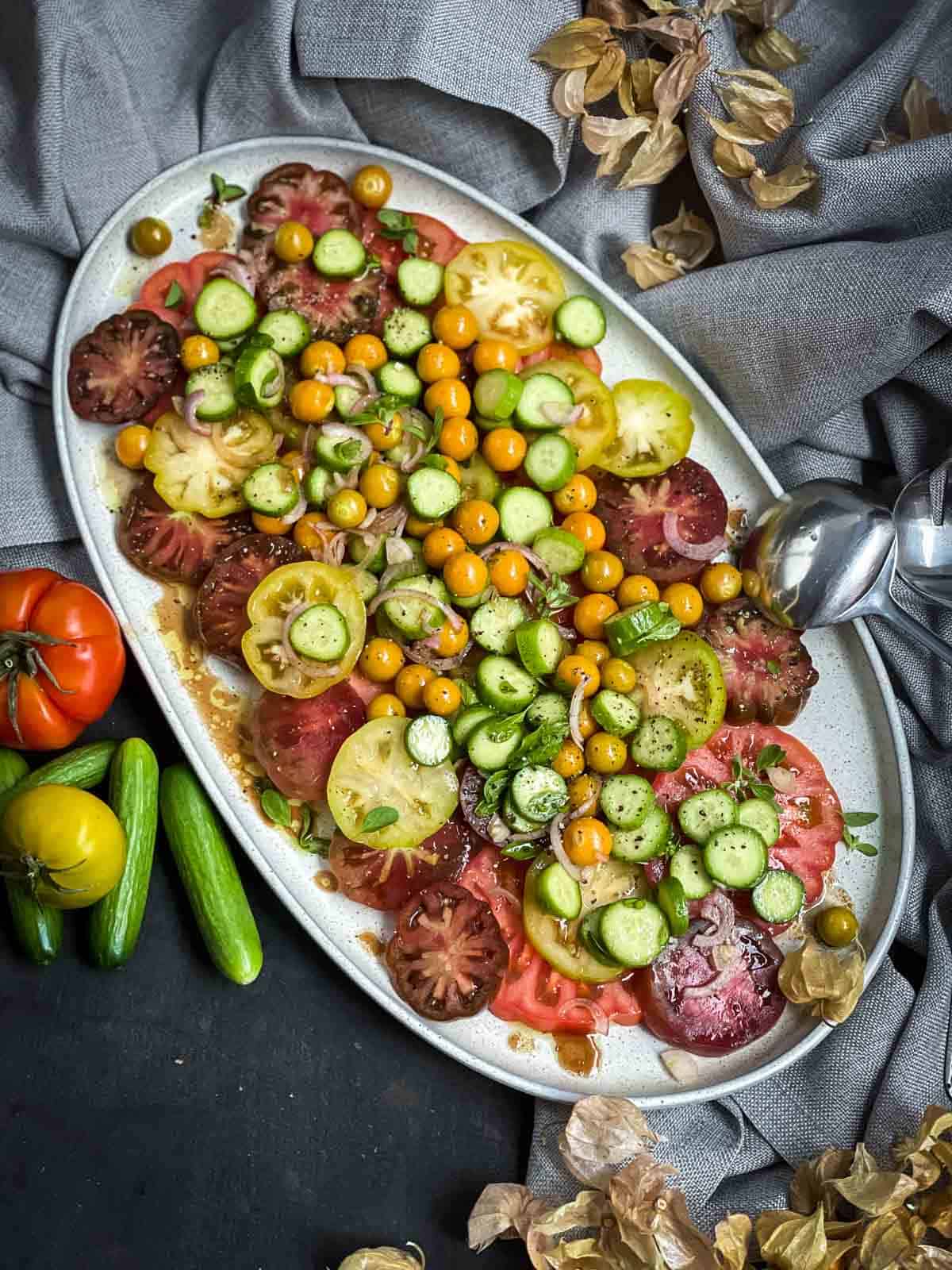 Baby Cucumber and Golden Berry Salad on a grey oval platter with silver salad spoon on grey weave linen