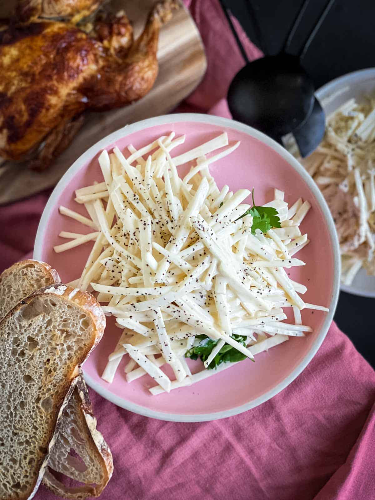 Celeri Remoulade on a pink plate served with whole roasted chicken and sliced bread