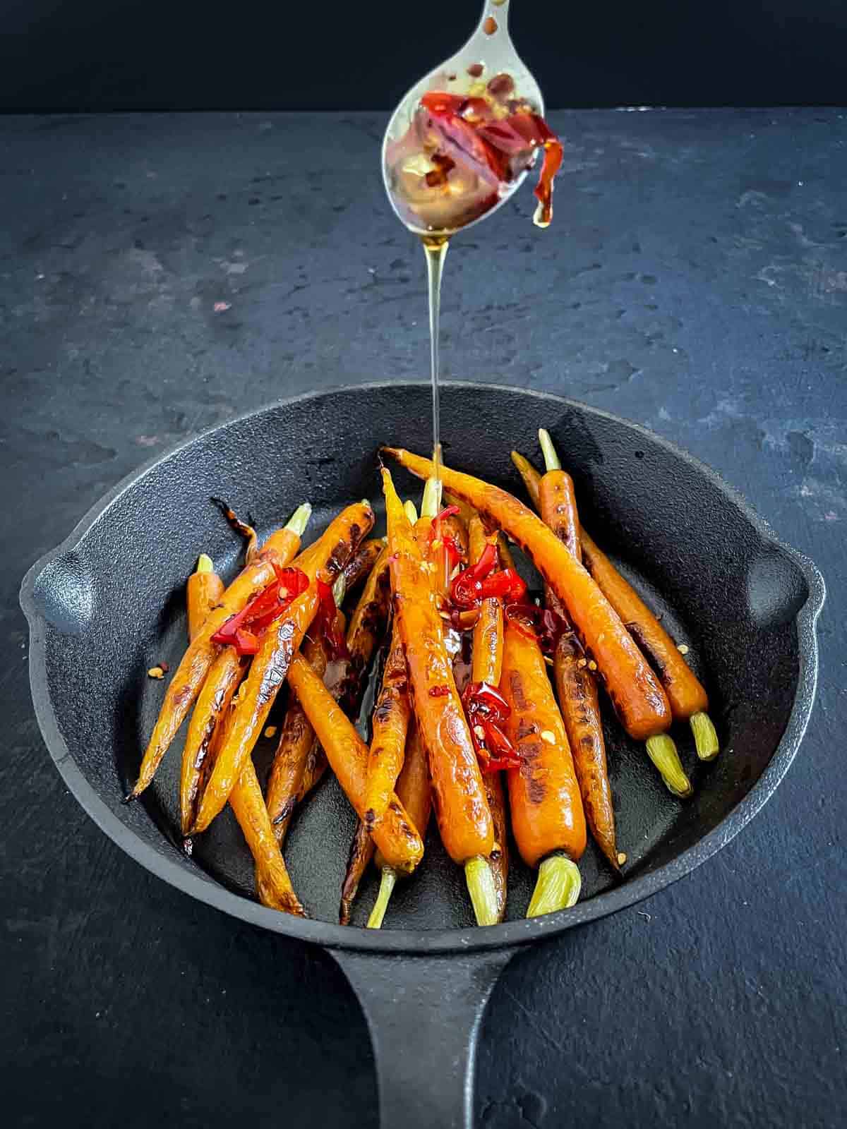 Drizzling hot honey onto sous vide carrots in a skillet