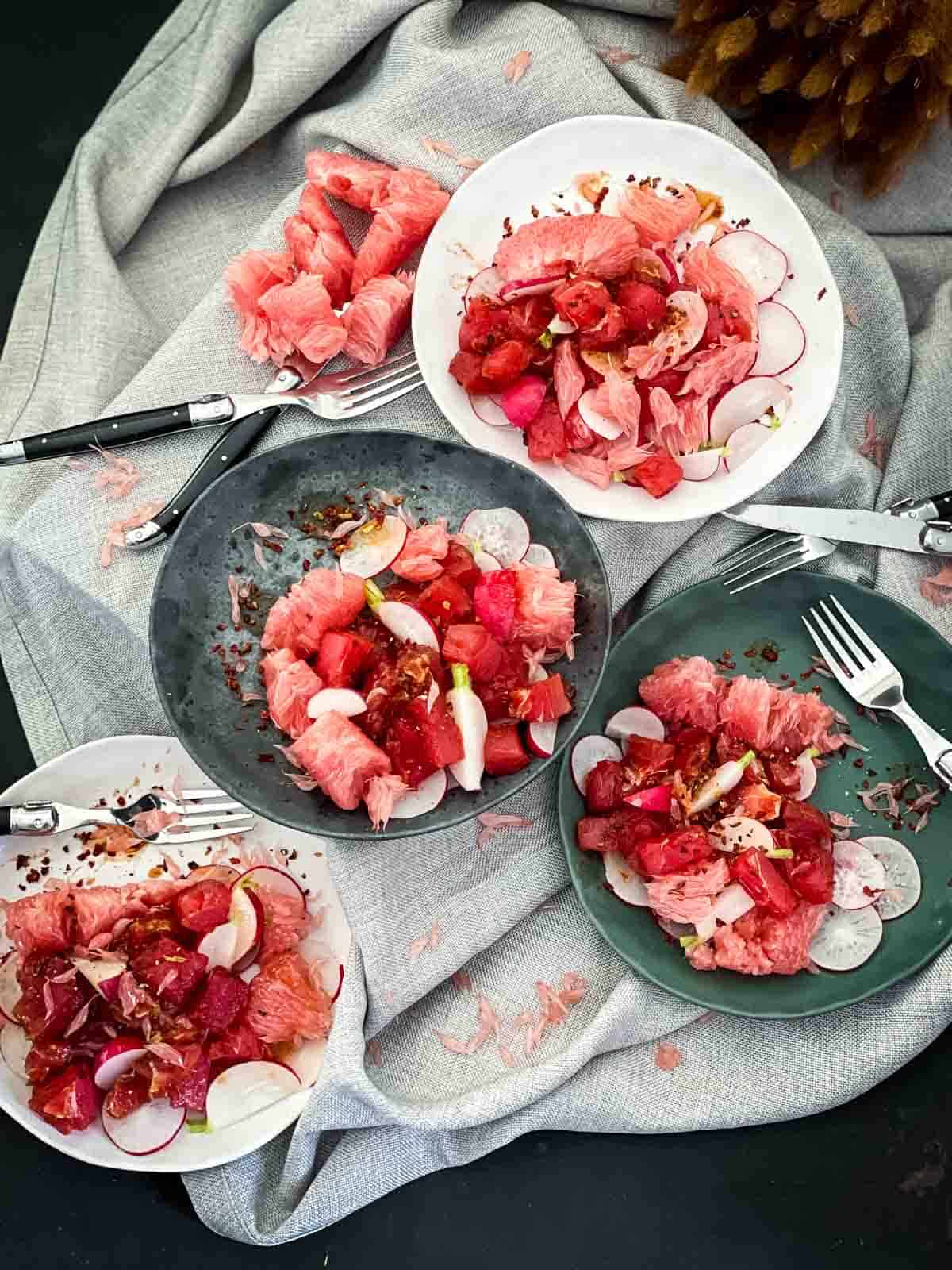 4 plates of Spicy Tuna Salad and Red Pomelo with black and silver cutlery on grey weave linen