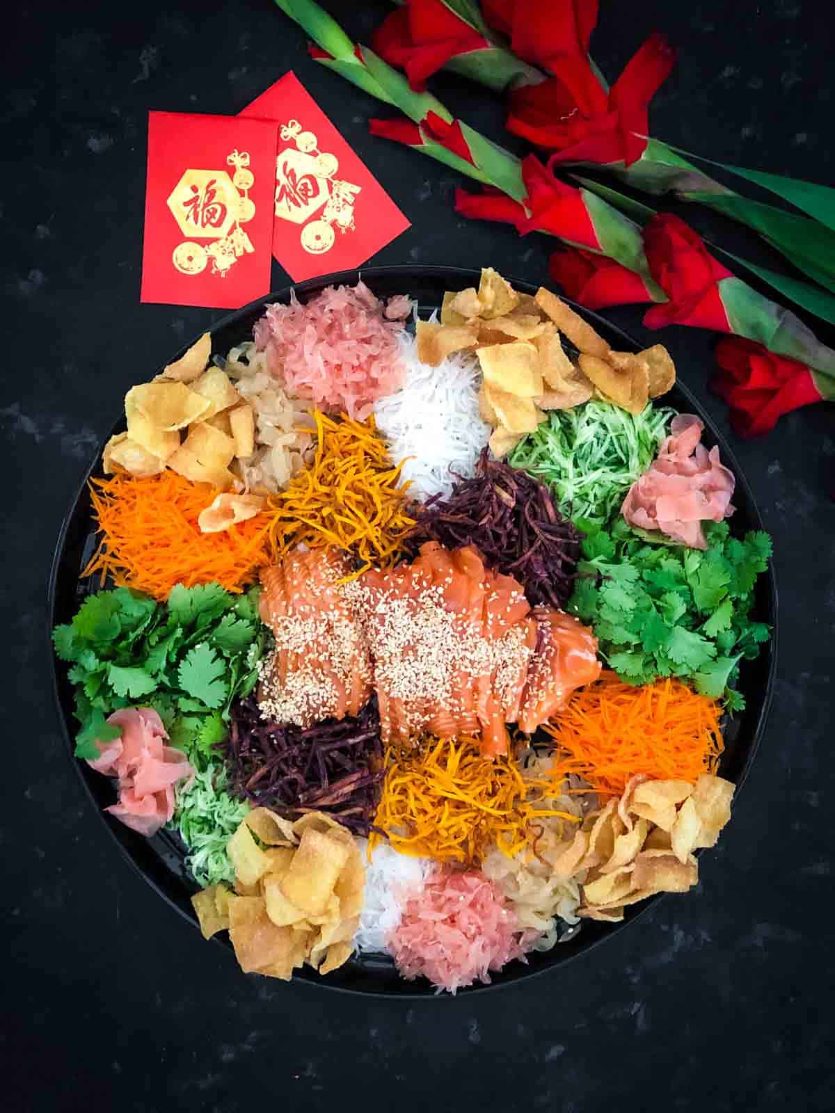 Yee sang platter decorated with Chinese red packets and red gladiolus flowers