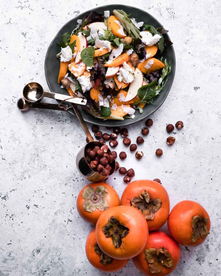 Persimmon Salad with hazelnuts in a measuring cup and whole persimmons