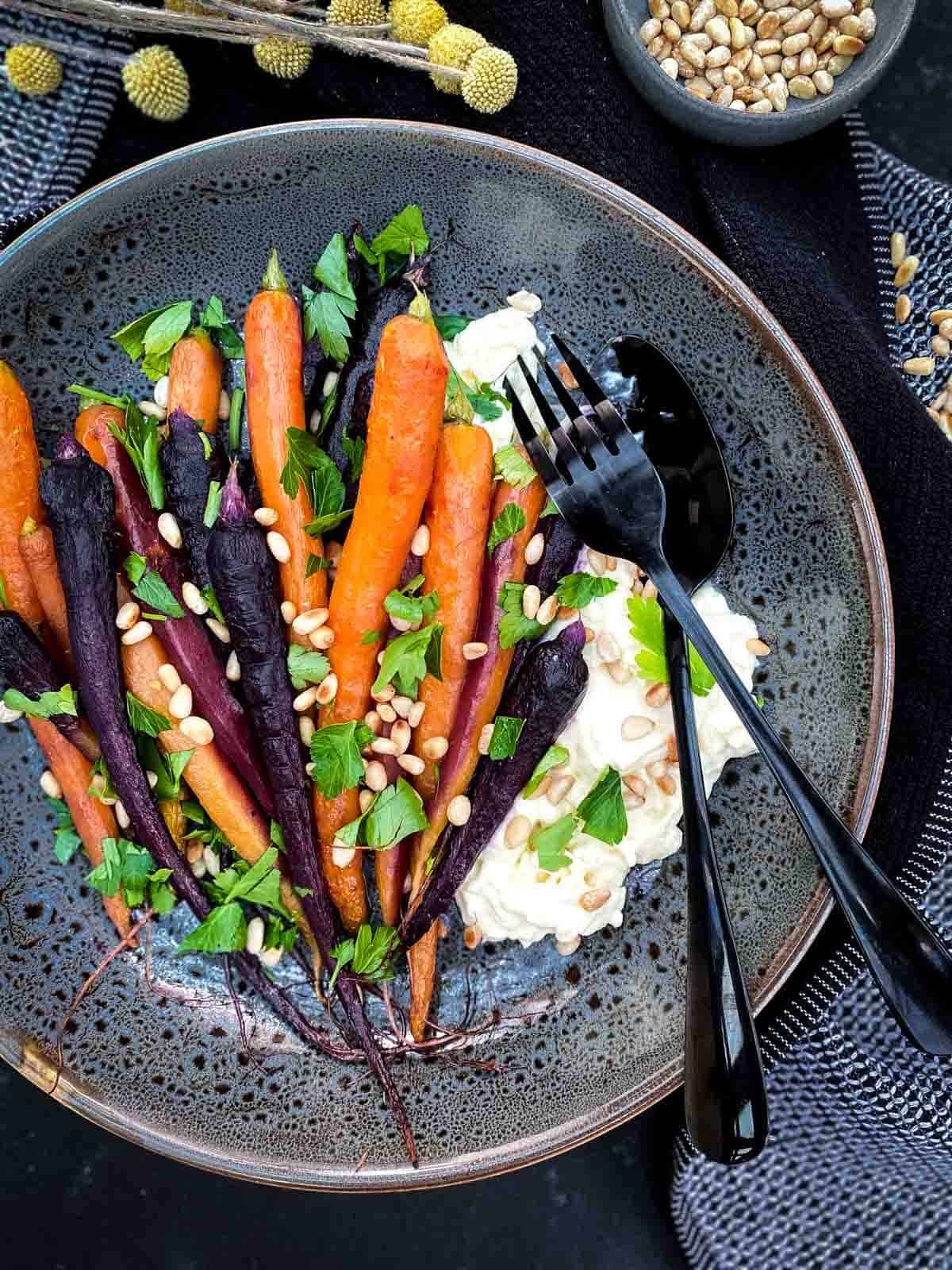 Roasted Maple Carrots with Stracciatella Cheese in a grey bowl with black cutlery on blue napery