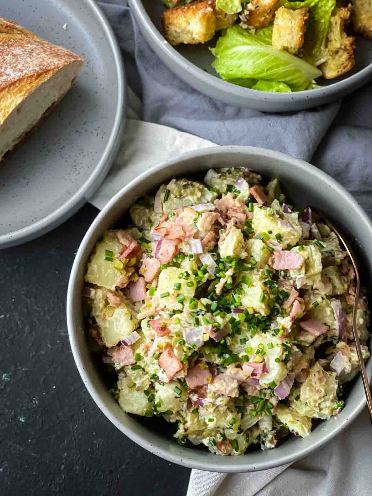 Potato salad in a large grey bowl served with fresh bread and lettuce side salad