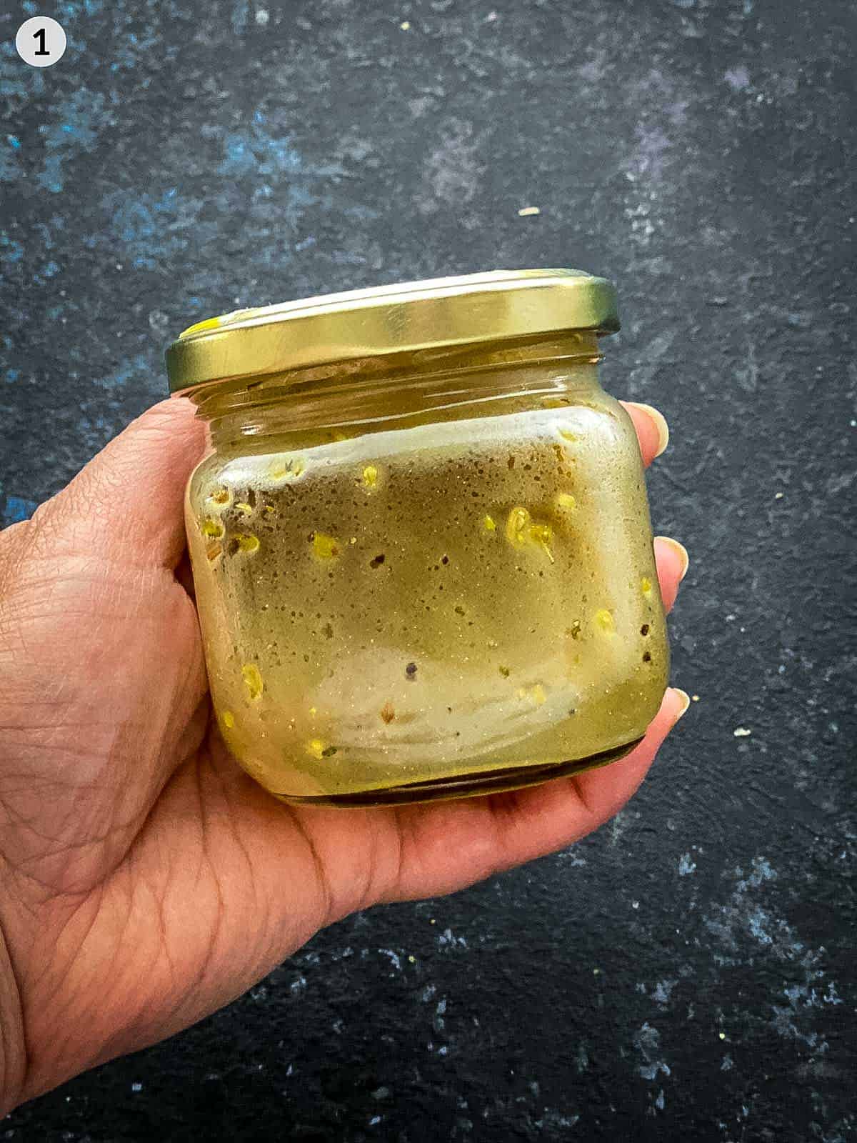 A hand holding a jar of oregano vinaigrette