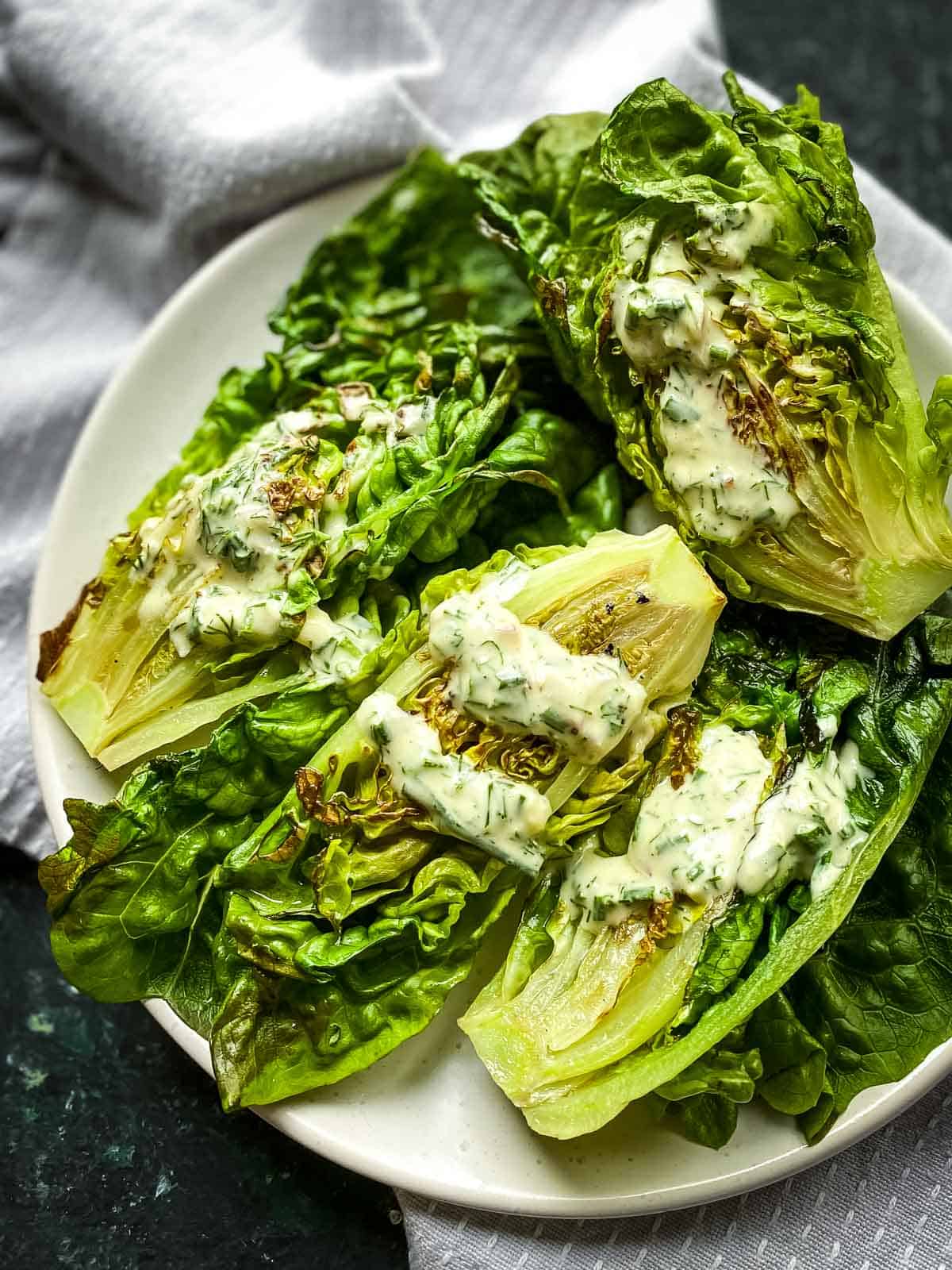 Grilled Little Gem Salad with Tahini Ranch Dressing served on a white plate over grey napery