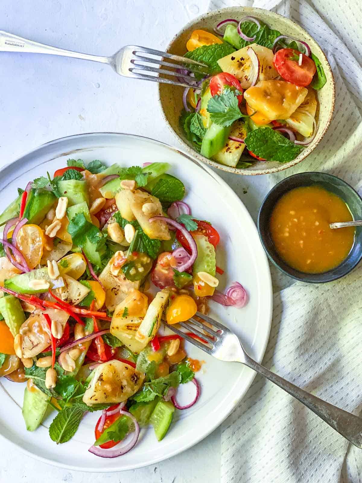 a fork holding a grilled pineapple piece with peanut dressing on the top