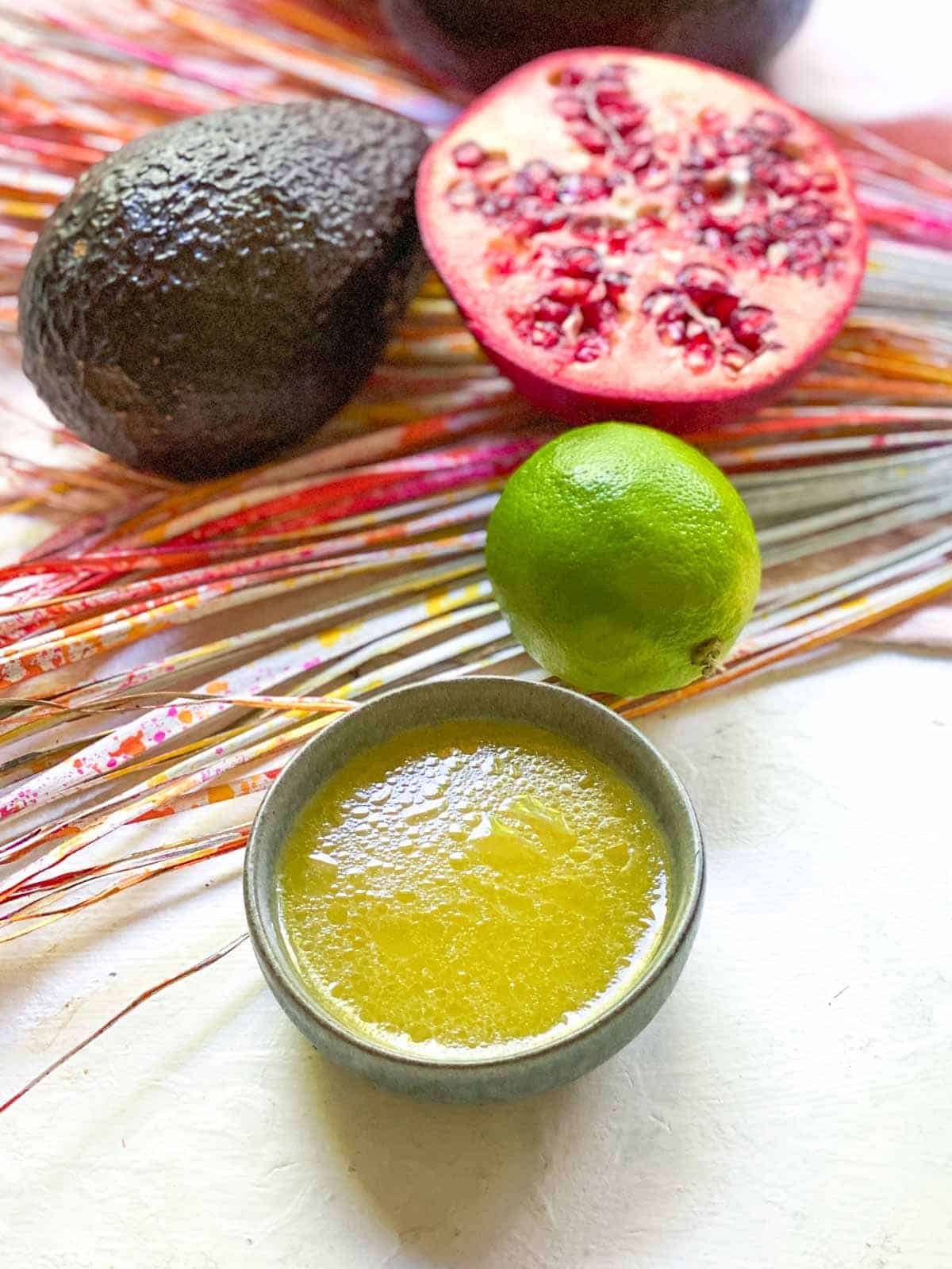 honey lime dressing in a small bowl with avocado, lime and pomegranate laying on a coloured leaf in the background