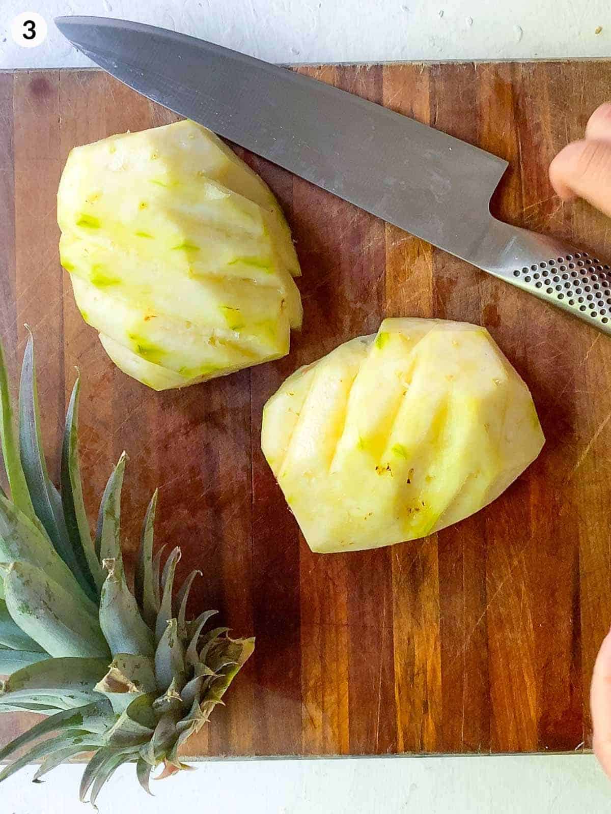 half of pineapple lying flat on wooden chopping board with diagonal cuts