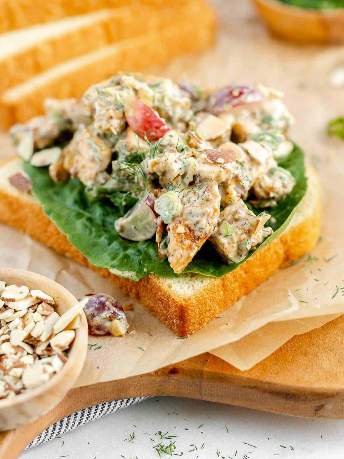 California chicken salad sandwich on a slice of bread on parchment paper