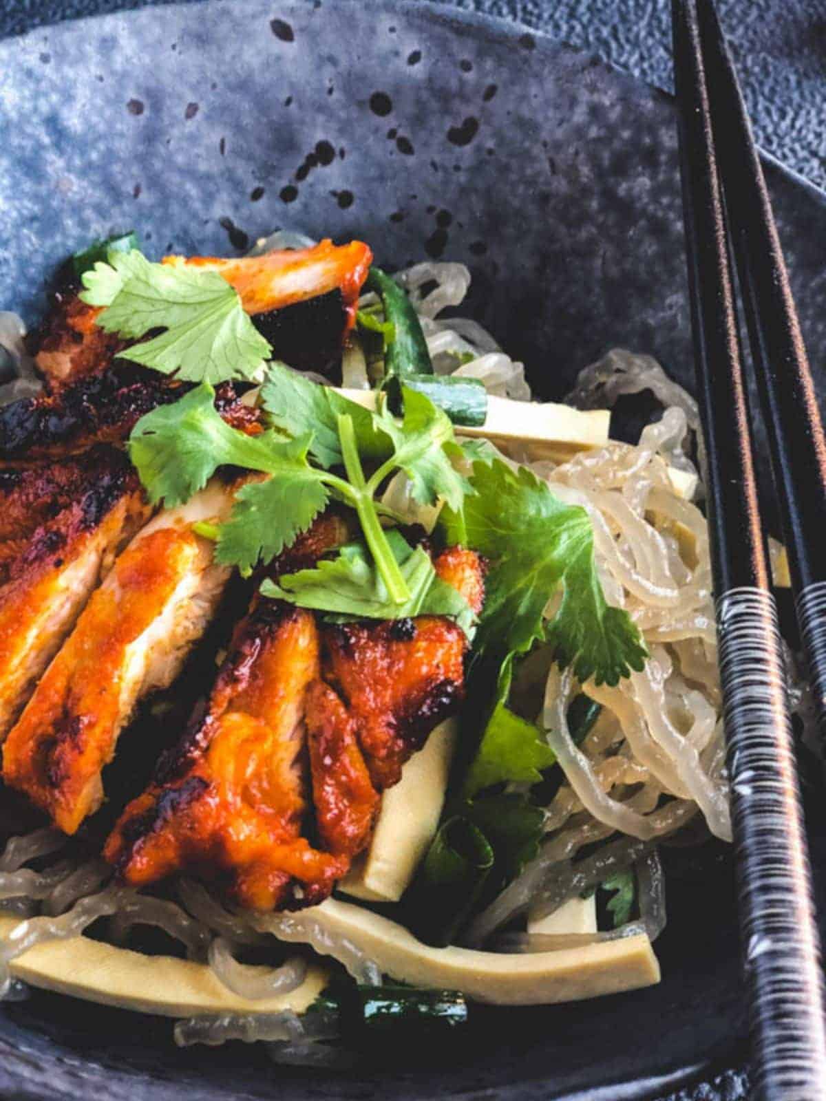 Gochujang chicken and potato noodle salad in a grey bowl and black chopsticks