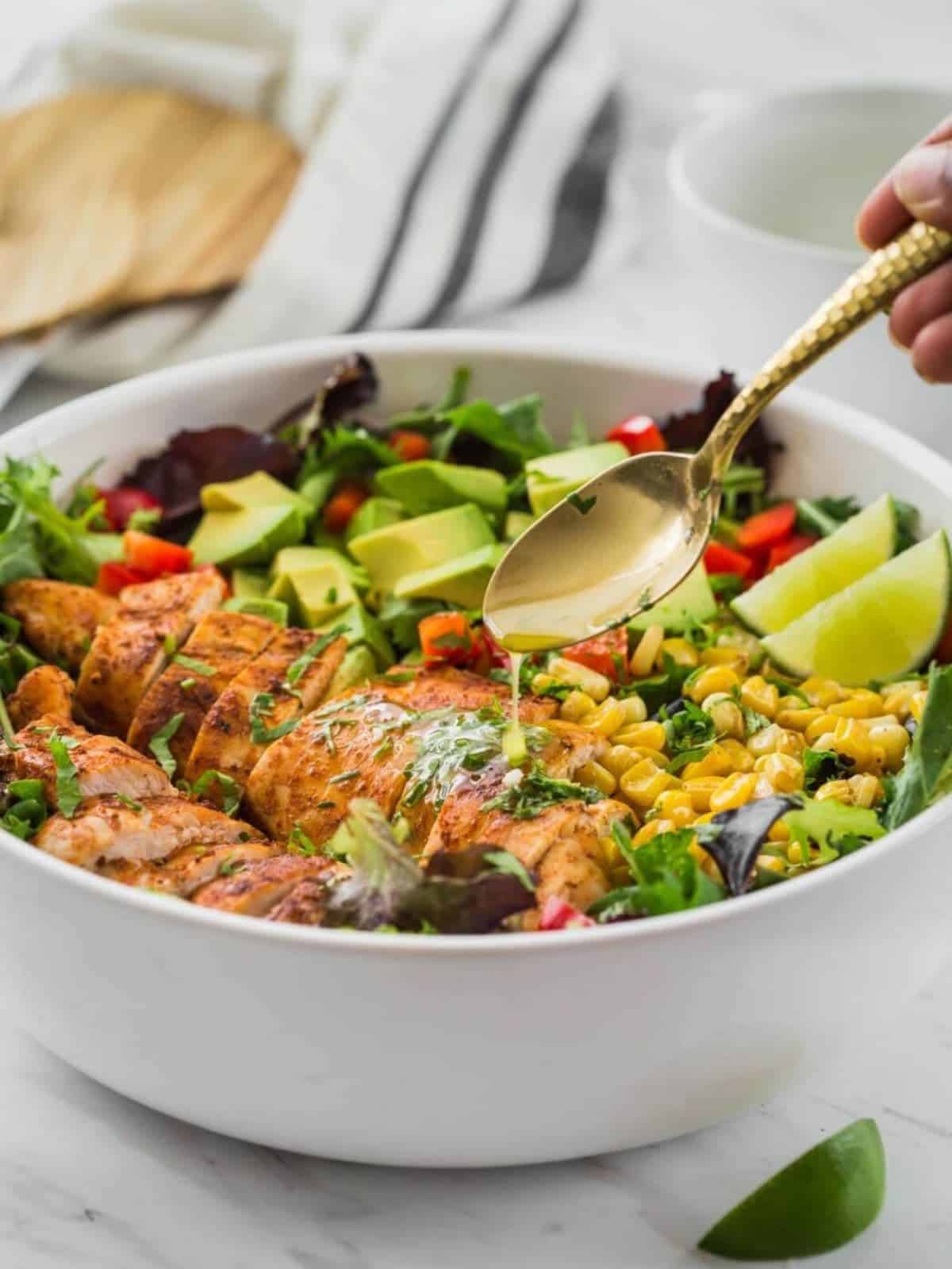 Pouring dressing from a spoon onto Mexican chicken avocado salad in a white bowl