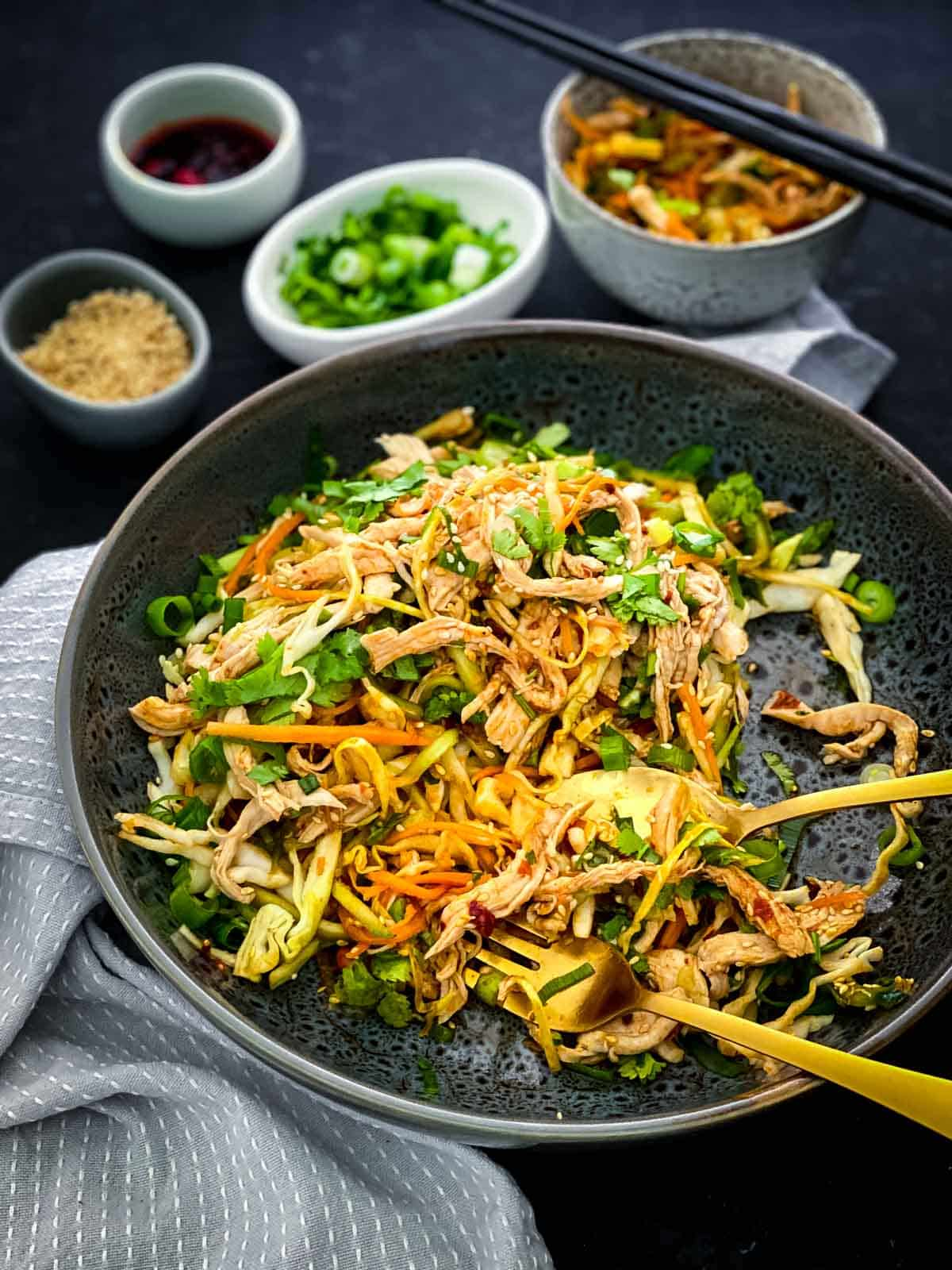 Spicy chicken salad on a black plate served with gold cutlery and condiments in the background