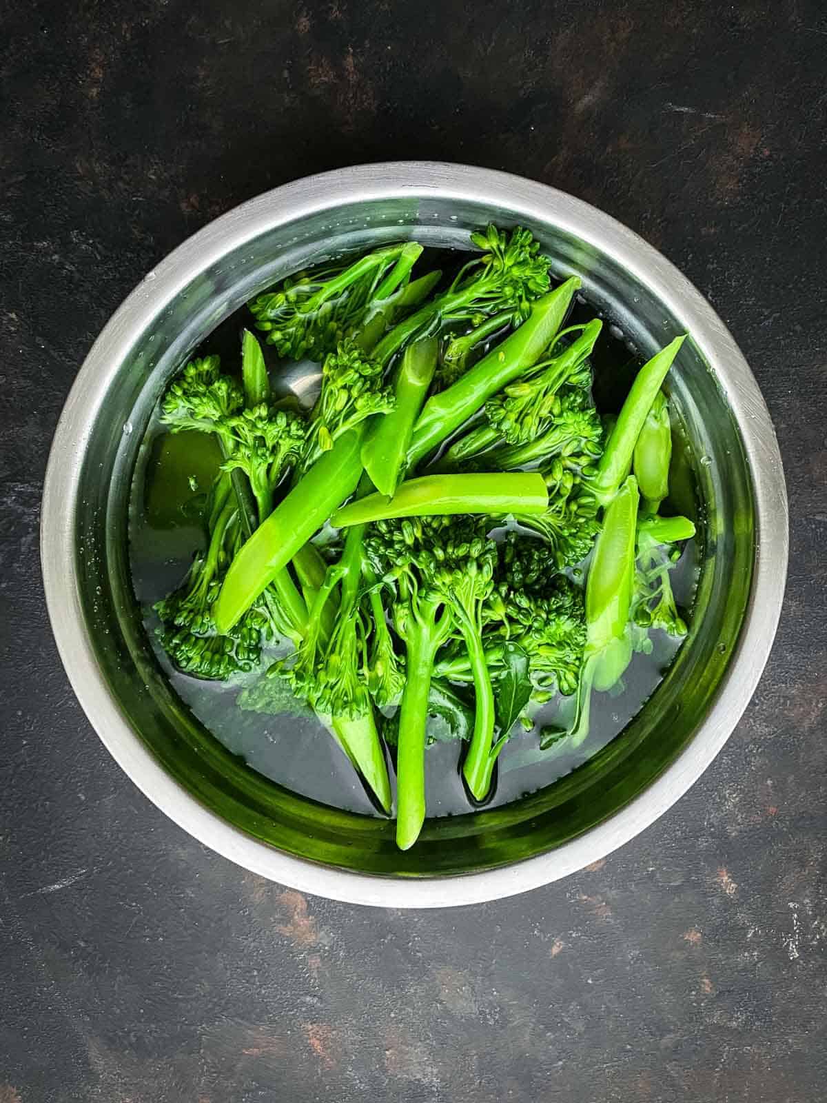 Placing blanched broccolini into a bowl of iced water to stop the cooking process.