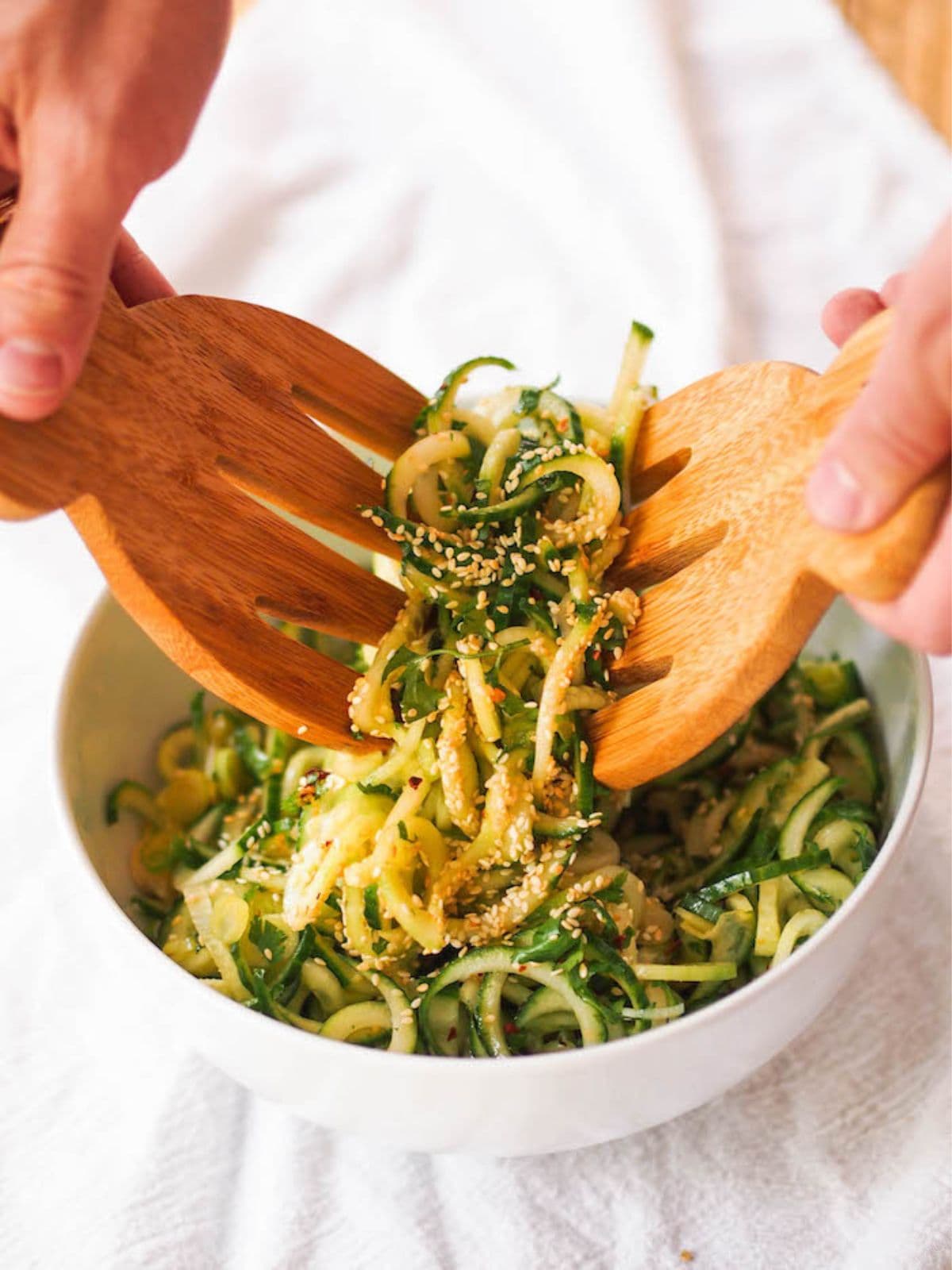 Hands using 2 wooden salad forks to lift a serve of spiralised cucumber salad