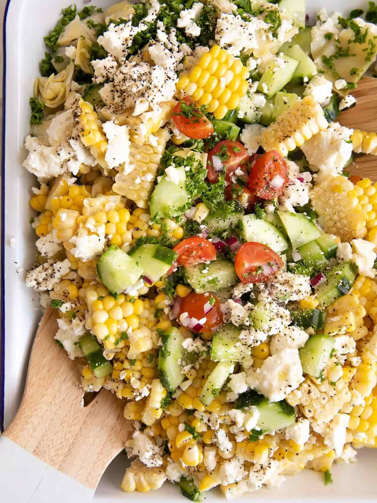 Corn salad with wooden salad server on a white platter