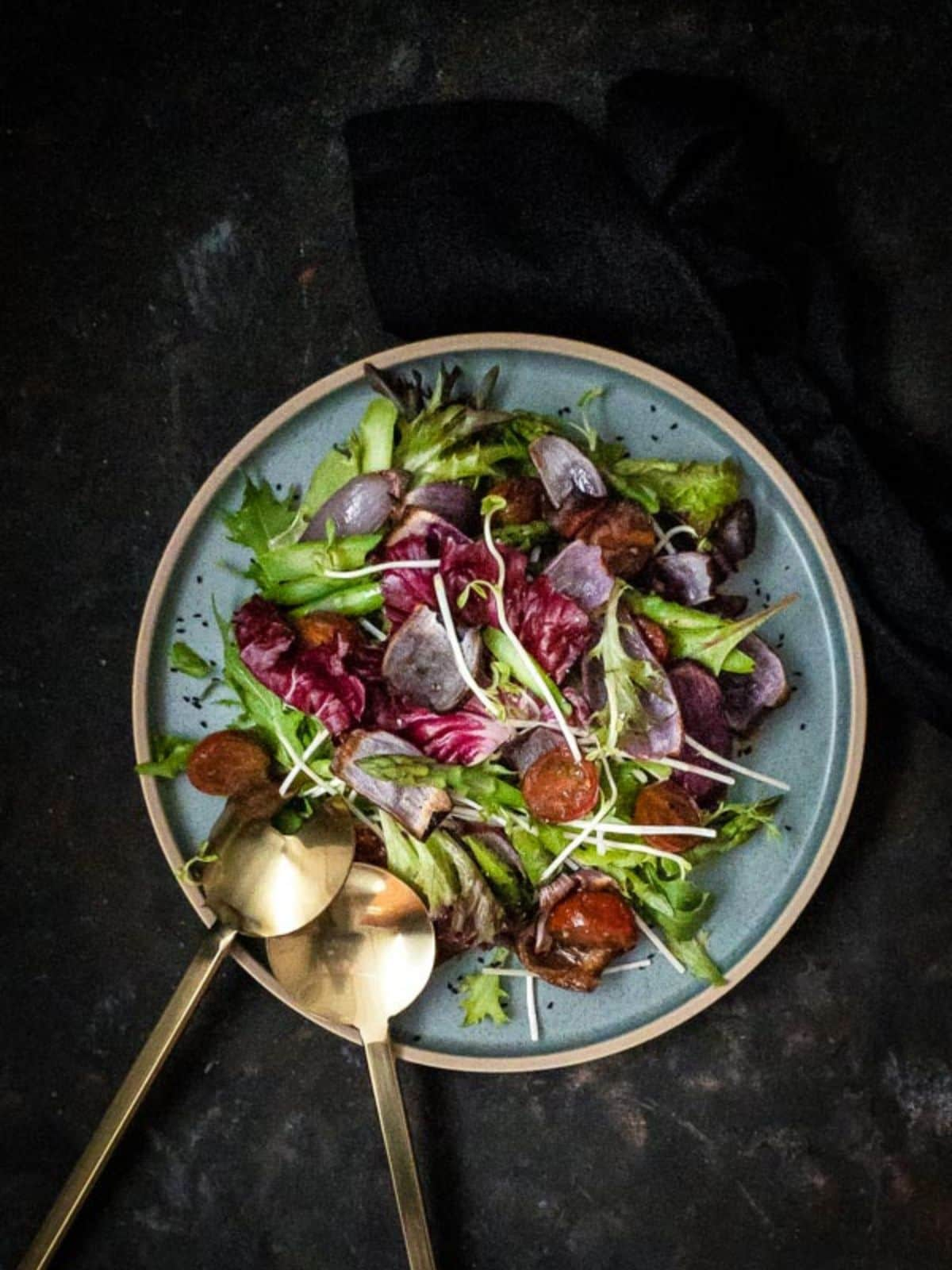 Roasted onion and asparagus salad in a blue bowl with gold salad servers