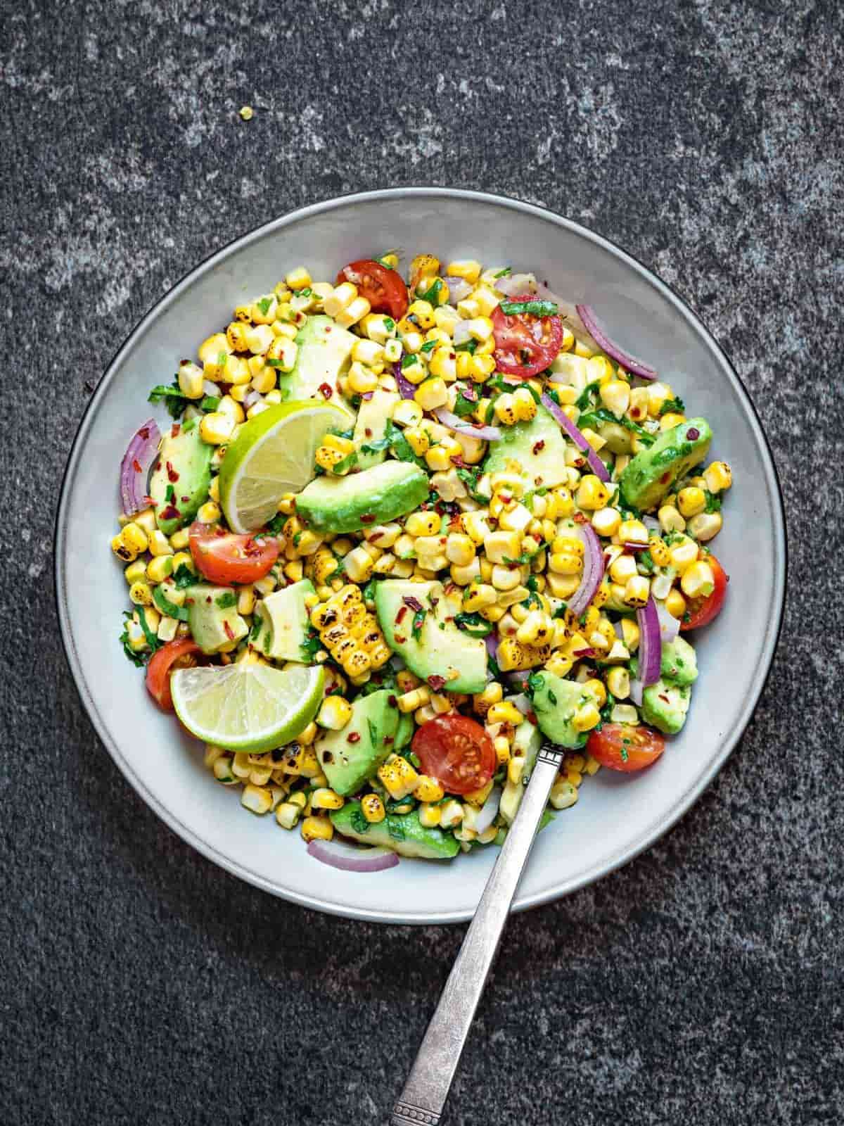 Tomato corn avocado salad in a grey bowl with a silver spoon