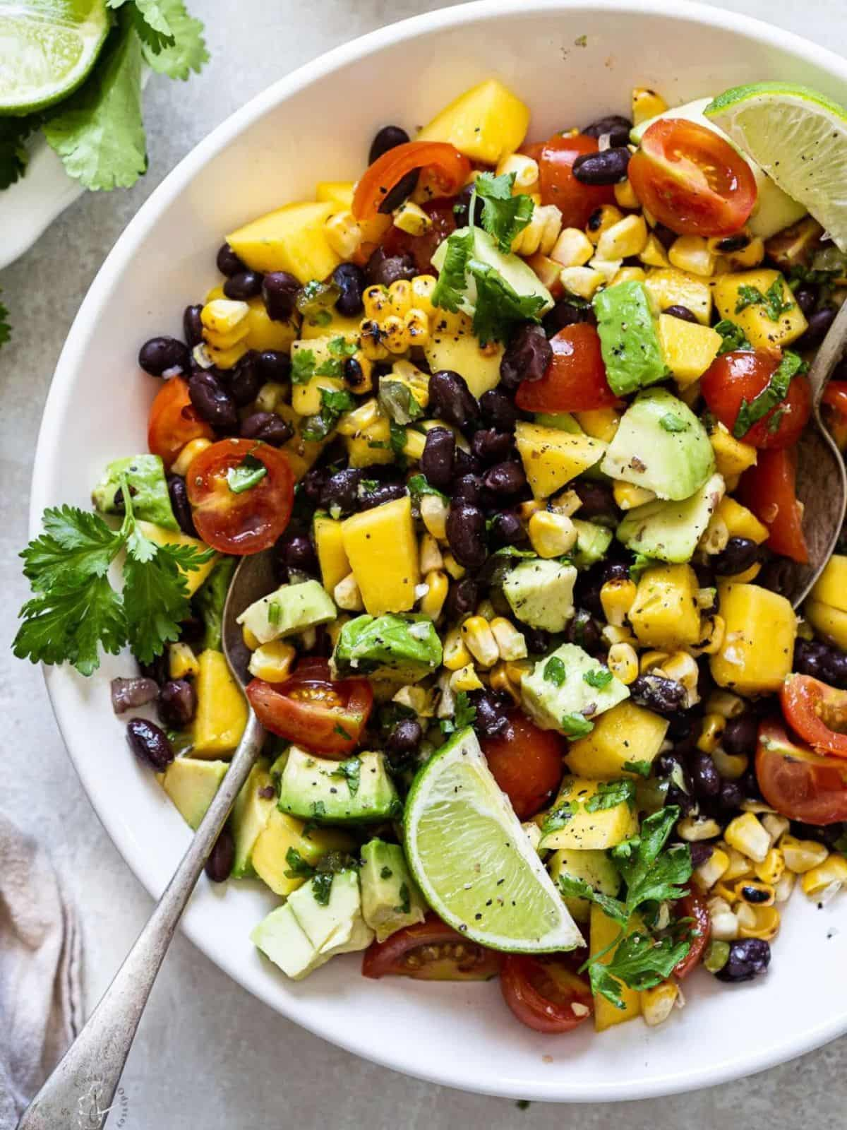 Black bean and mango salad in a white bowl with a spoon