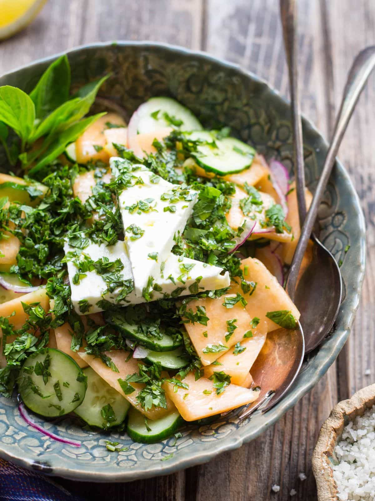 cucumber melon salad in a patterns blue bowl with fork and spoon on a rustic wooden table