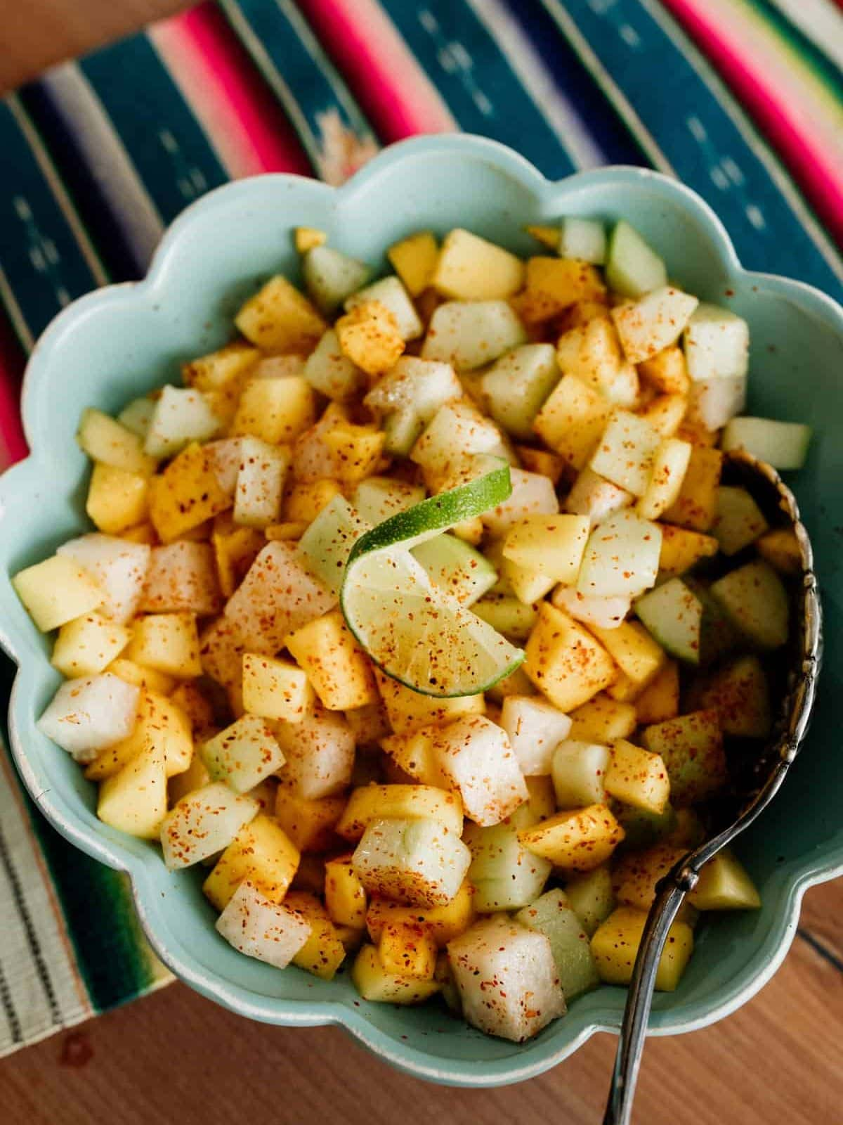 mango cucumber fruit salad in a flower shaped green bowl with a spoon