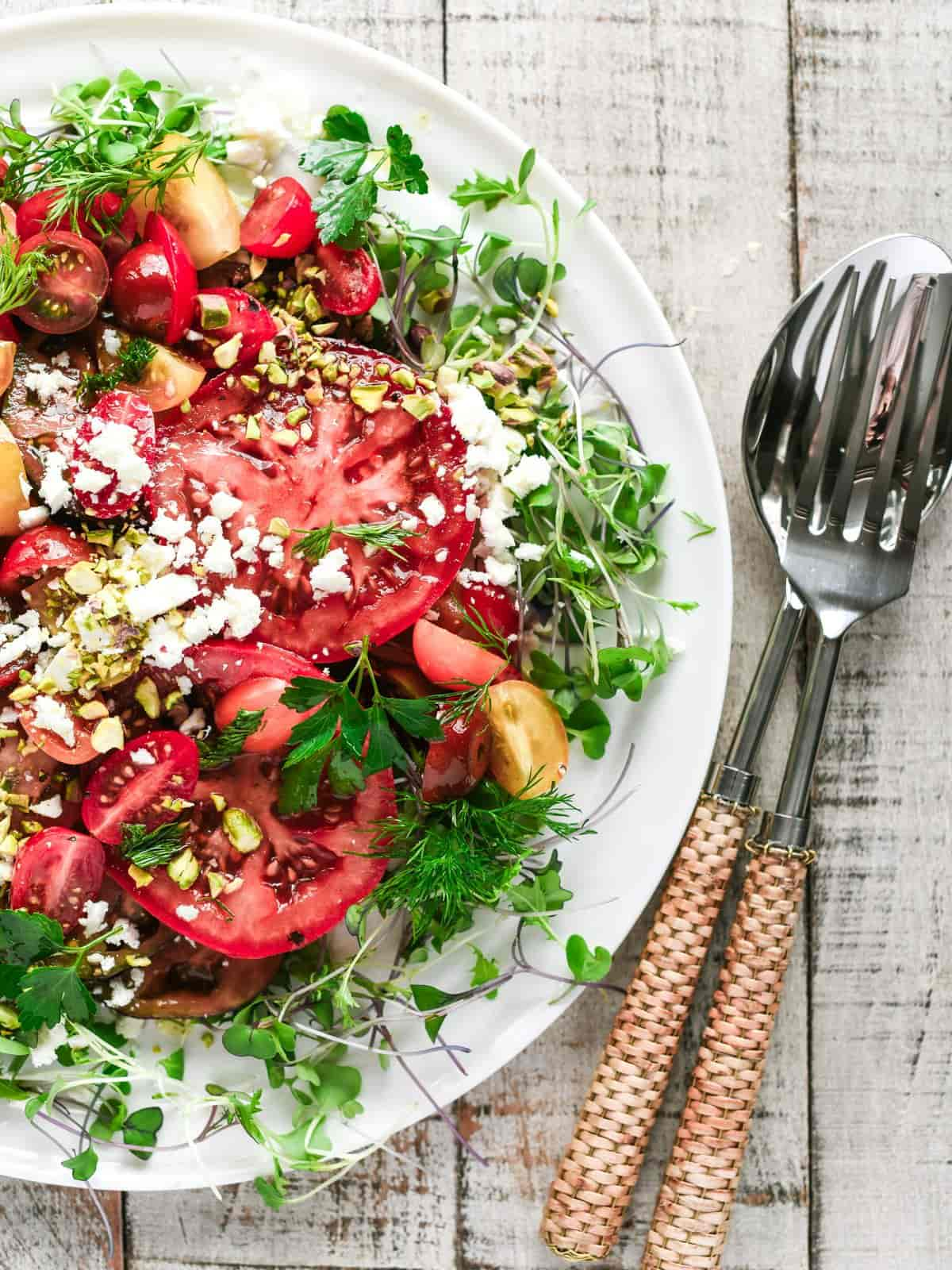 Marinated tomato salad on a white plate with rattan cutlery on the side