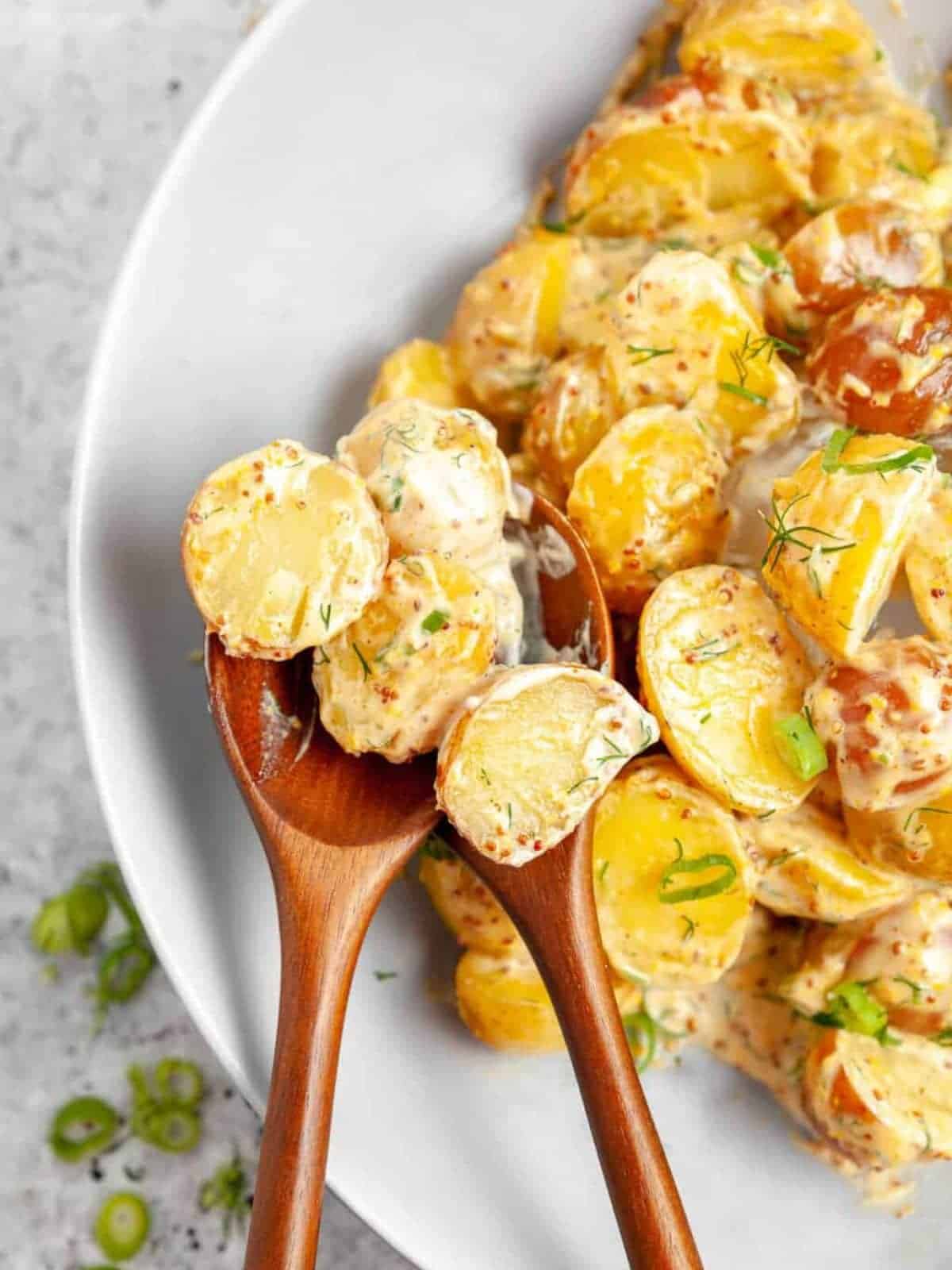 Mustard dill potato salad served on a white plate an wooden salad servers