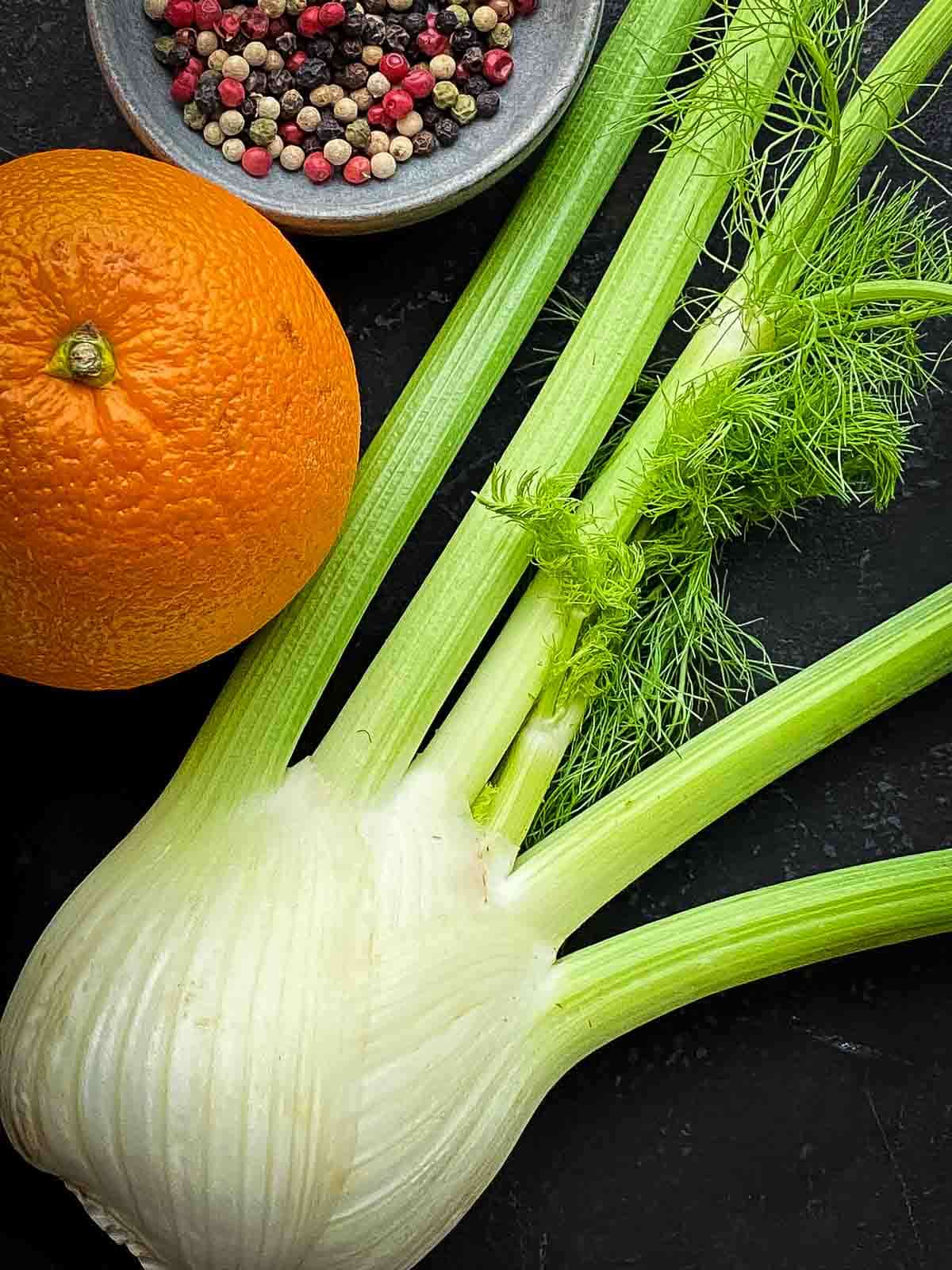 a fennel bulb next to orange and a bowl of rainbow peppercorns