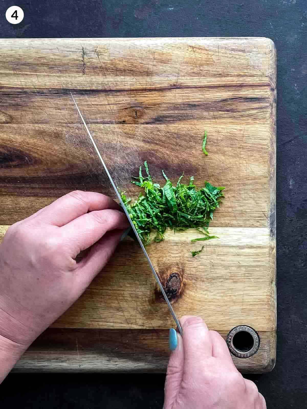 hand chopping mint leaves on a wooden chopping board