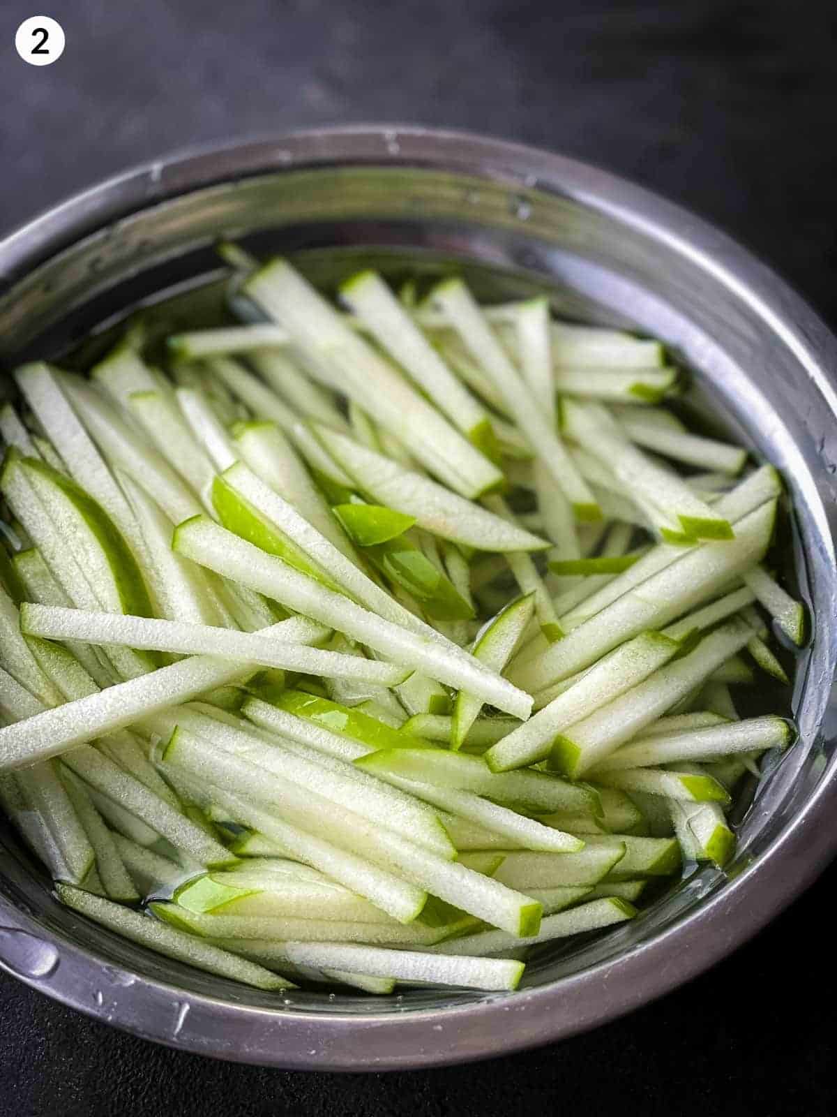 a bowl of green apple matchsticks in a salted water