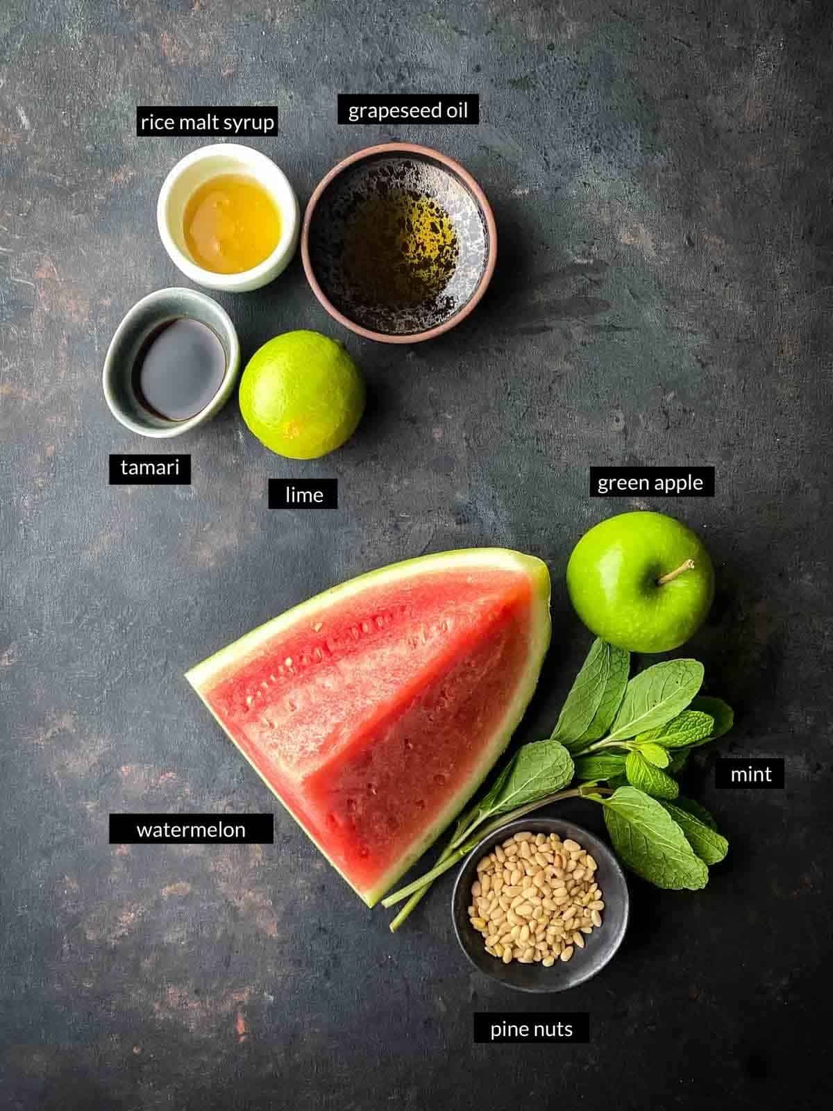 salad ingredients with watermelon, apple, mint and pine nuts next to dressing ingredients tamari, lime, syrup and oil