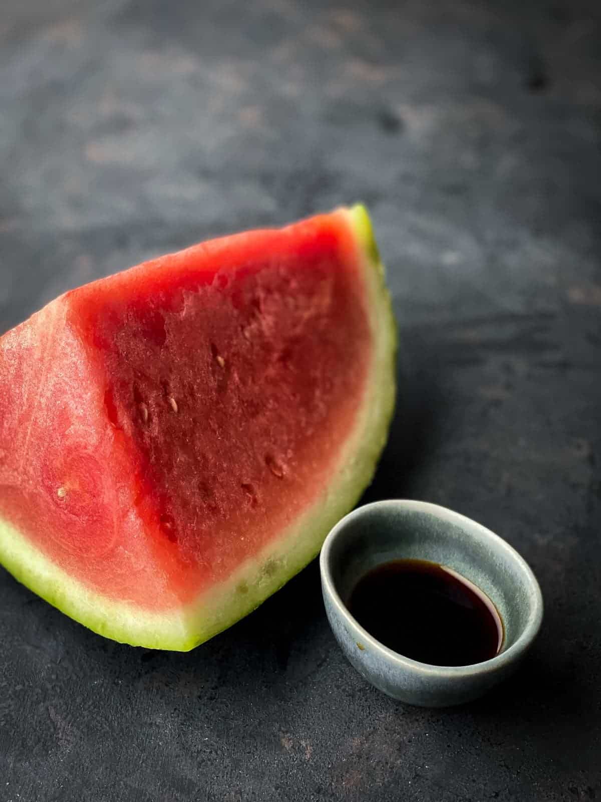 a cut piece of watermelon next a small bowl of tamari