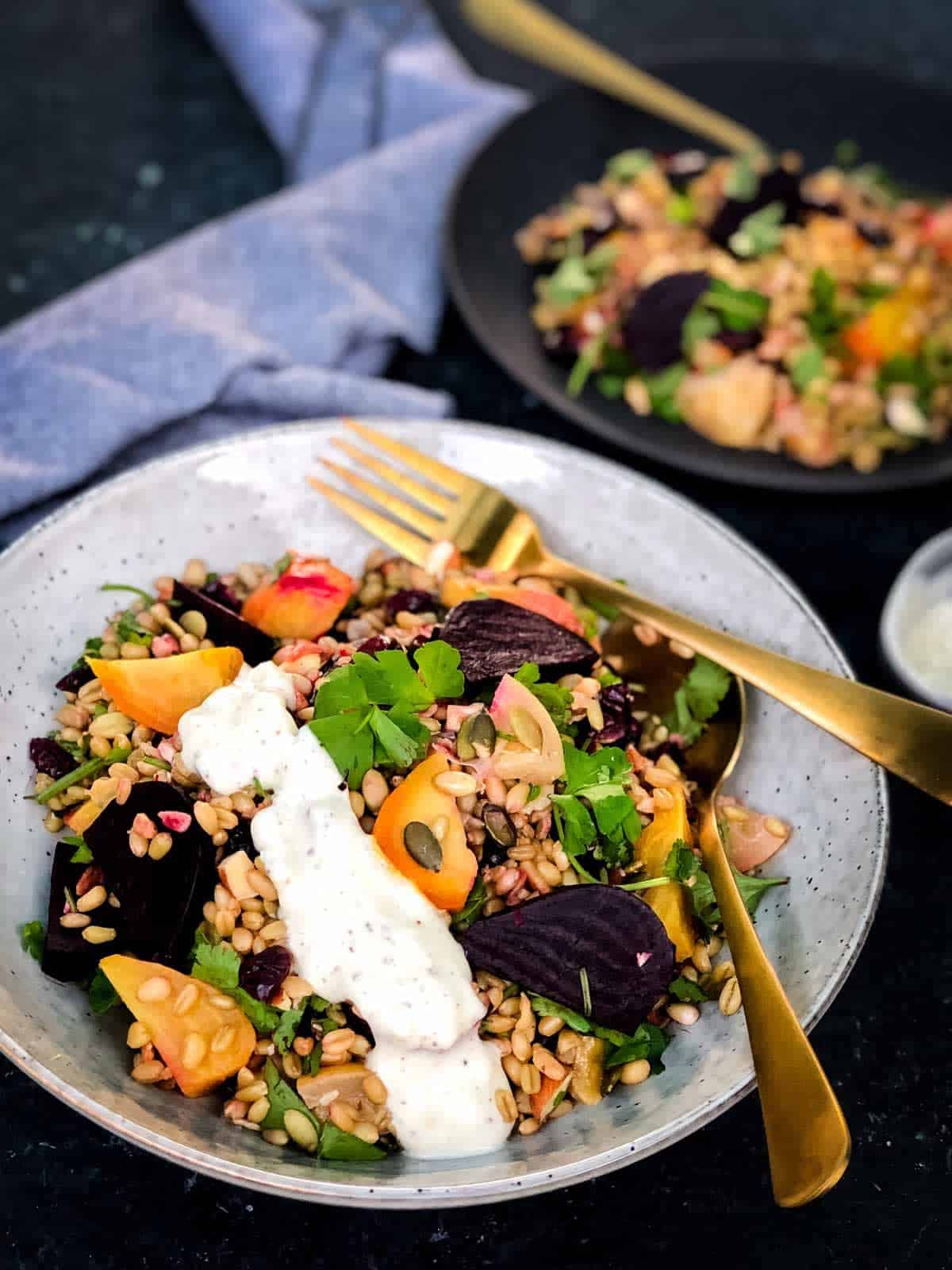 a bowl of freekeh grain salad with roasted beetroot and spiced sumac dressing drizzled on the side. Using gold fork and spoon to serve.