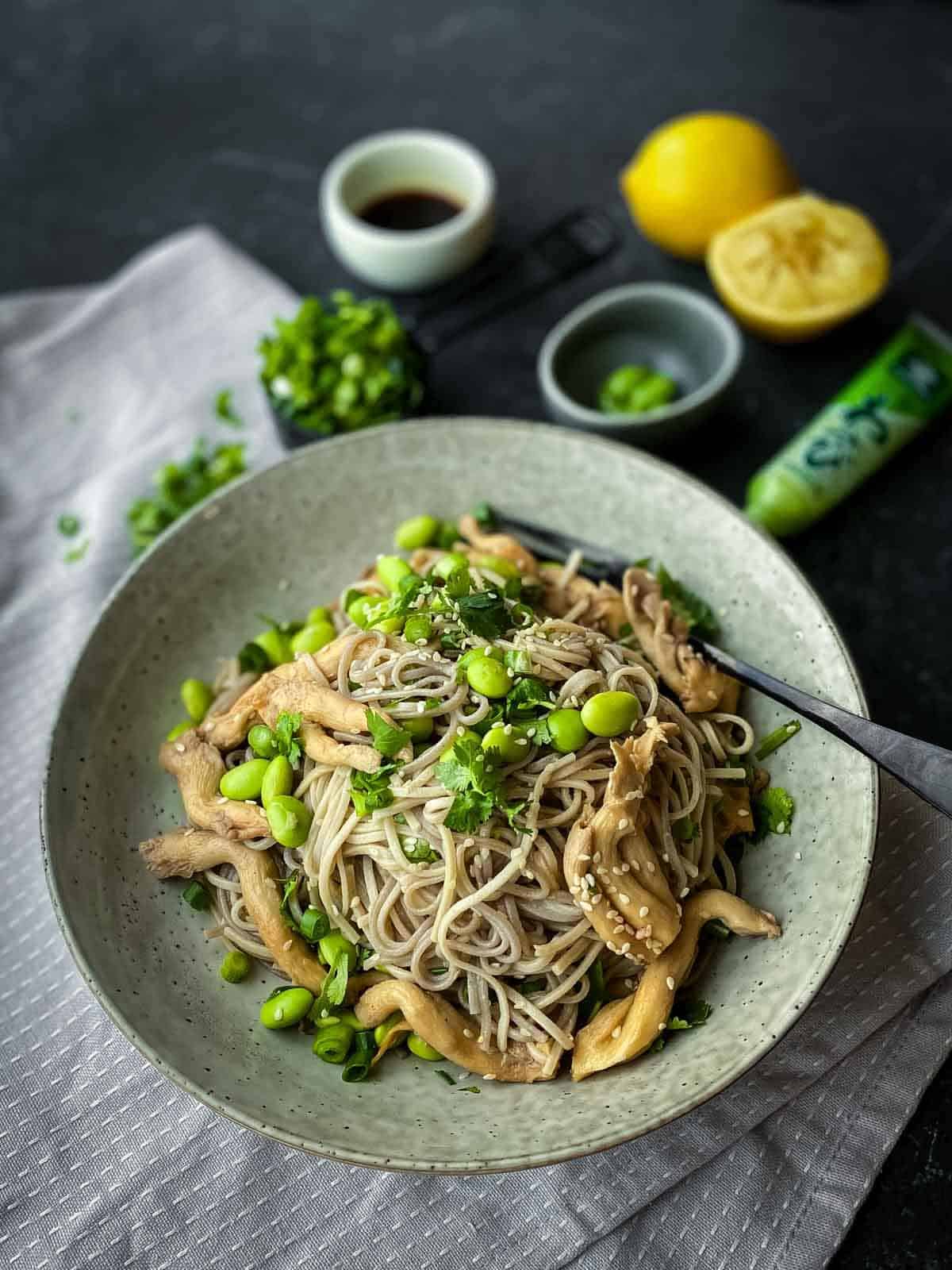 soba noodles, pearl mushrooms, edamame, spring onions, cilantro and sesame seeds served in a grey bowl with fork on side