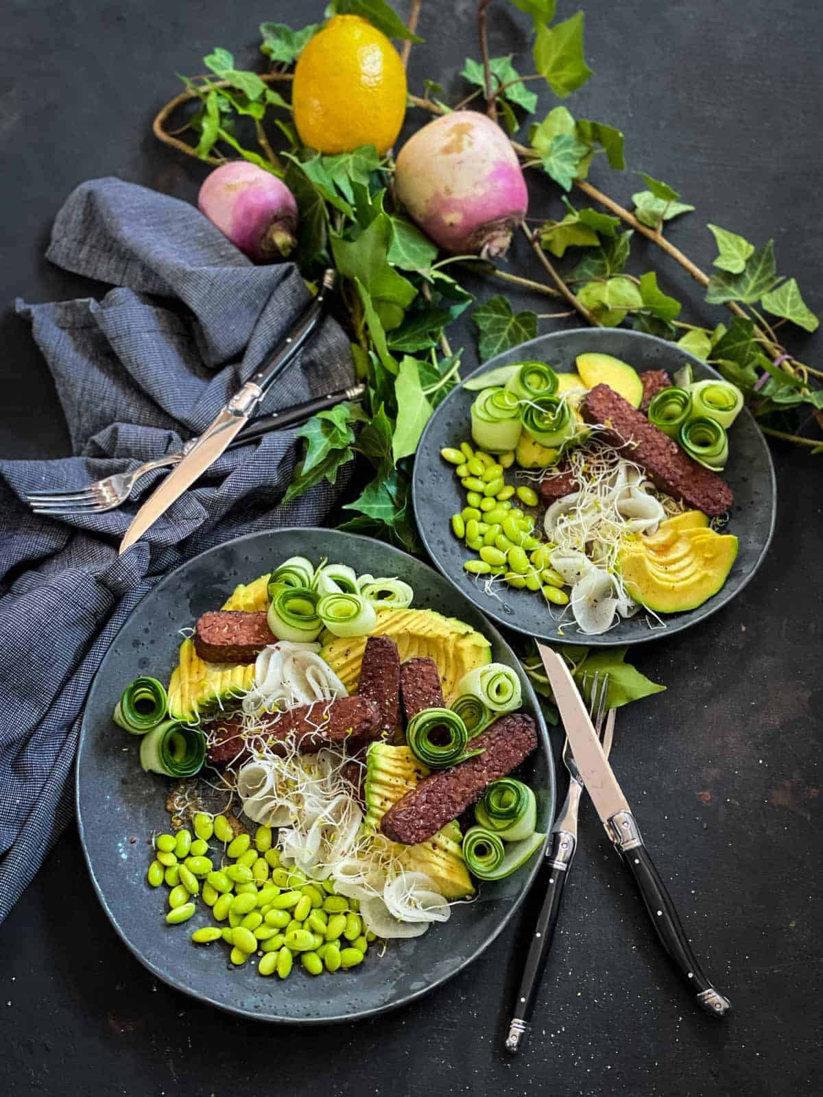 2 serves of Baked Tempeh Salad with blue napkins, black and silver cutlery and vines