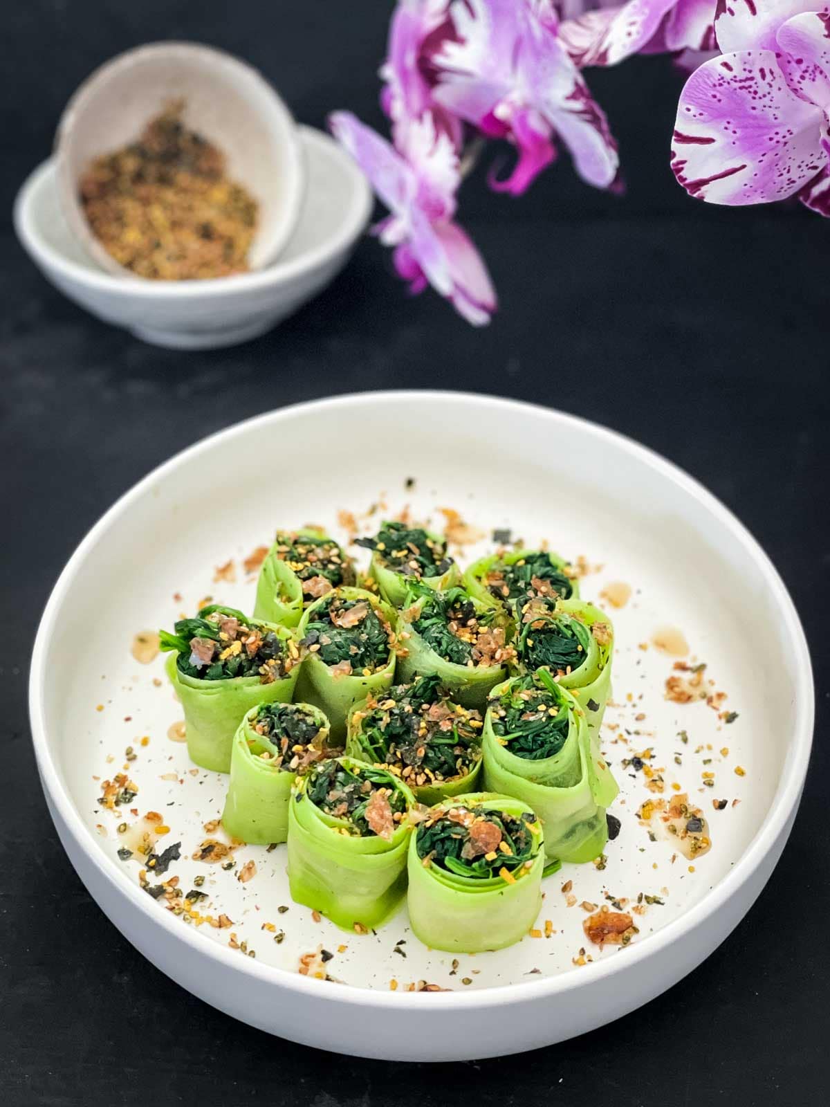 Chinese Squash and Spinach Rolls in a white salad bowl with orchids and a bowl of furikake in the background