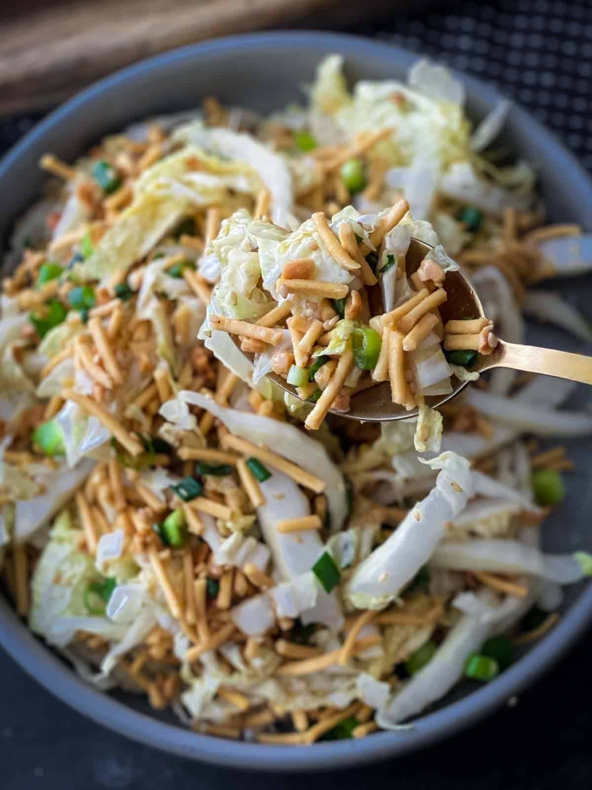 spoon scooping crunchy noodle salad on top a big bowl of salad