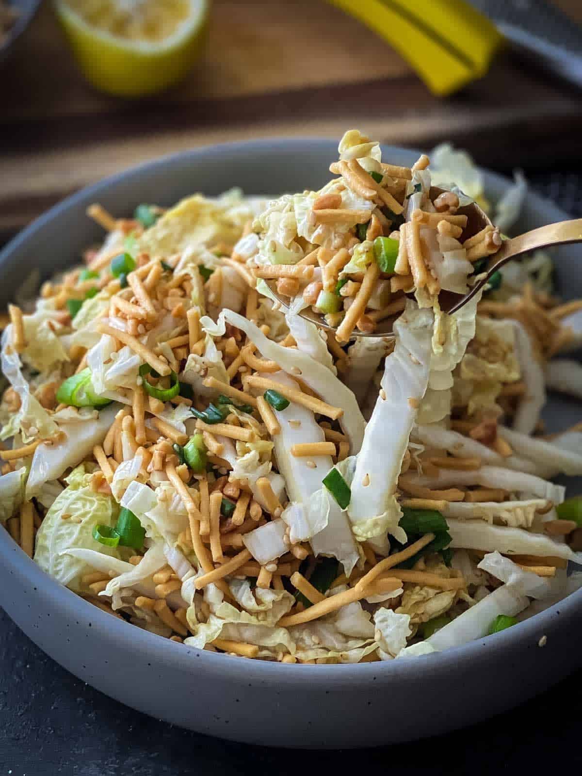 crunchy noodle salad with wombok in a round grey bowl with serving spoon on the right