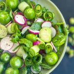 Radish and Tomatillo Salad on a green plate hovering over fresh whole tomatillos